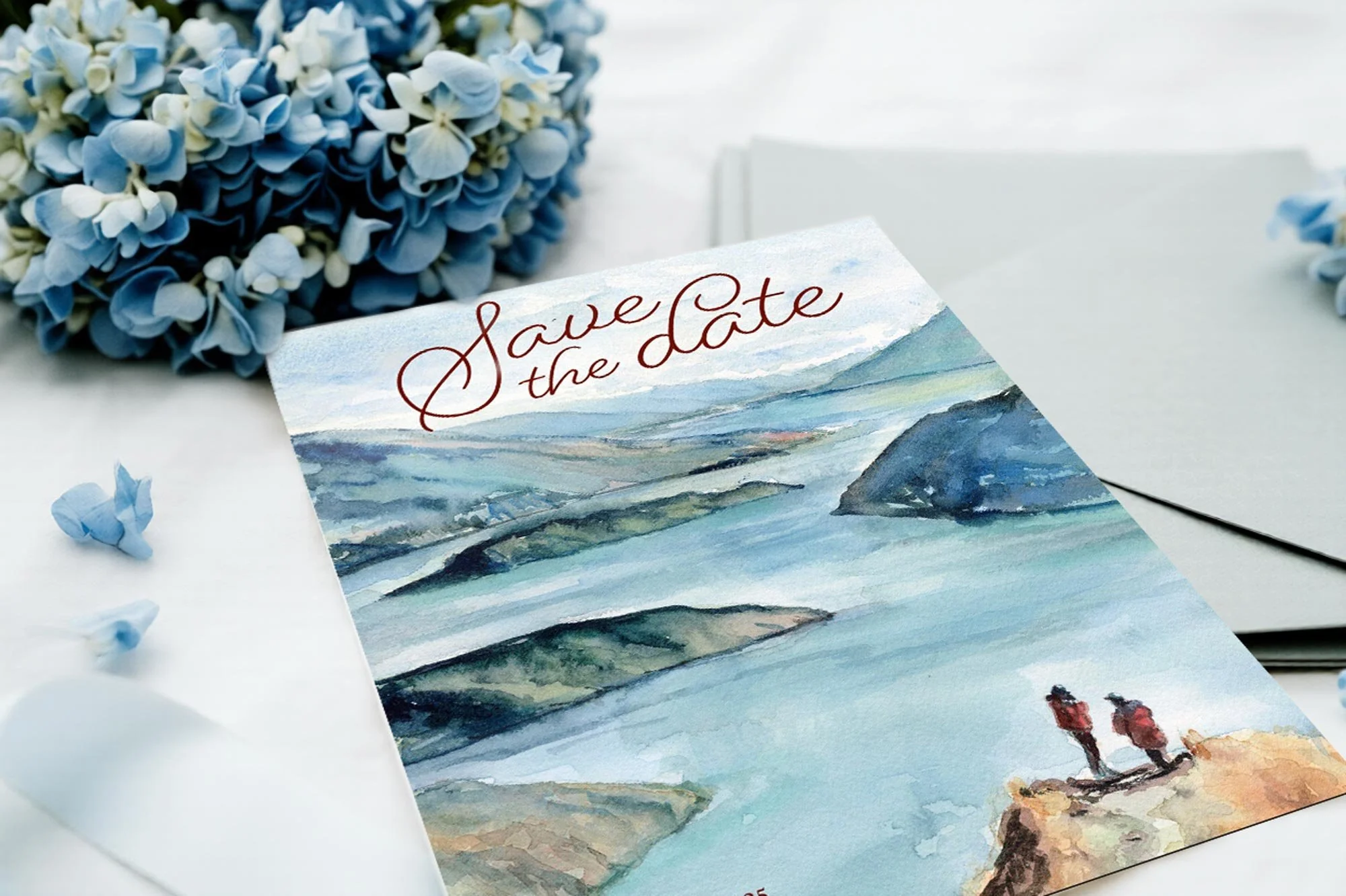 Save the date card with landscape watercolor painting of mountains and water, two people standing on a rocky cliff, and blue hydrangea flowers nearby.