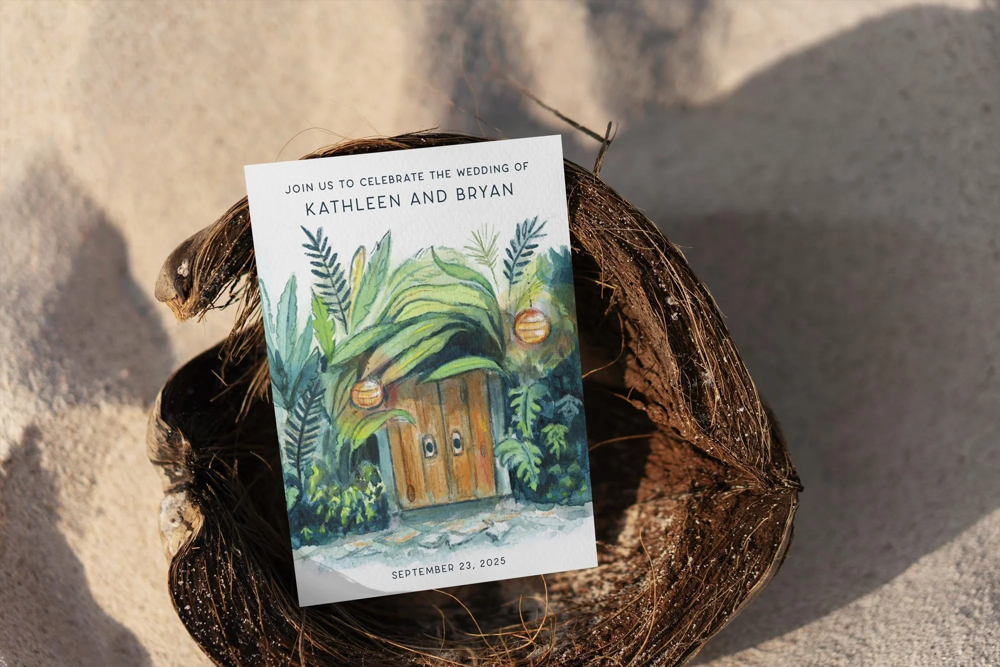 Wedding invitation card with watercolor illustration of a door surrounded by greenery, placed inside a coconut shell on sandy ground.