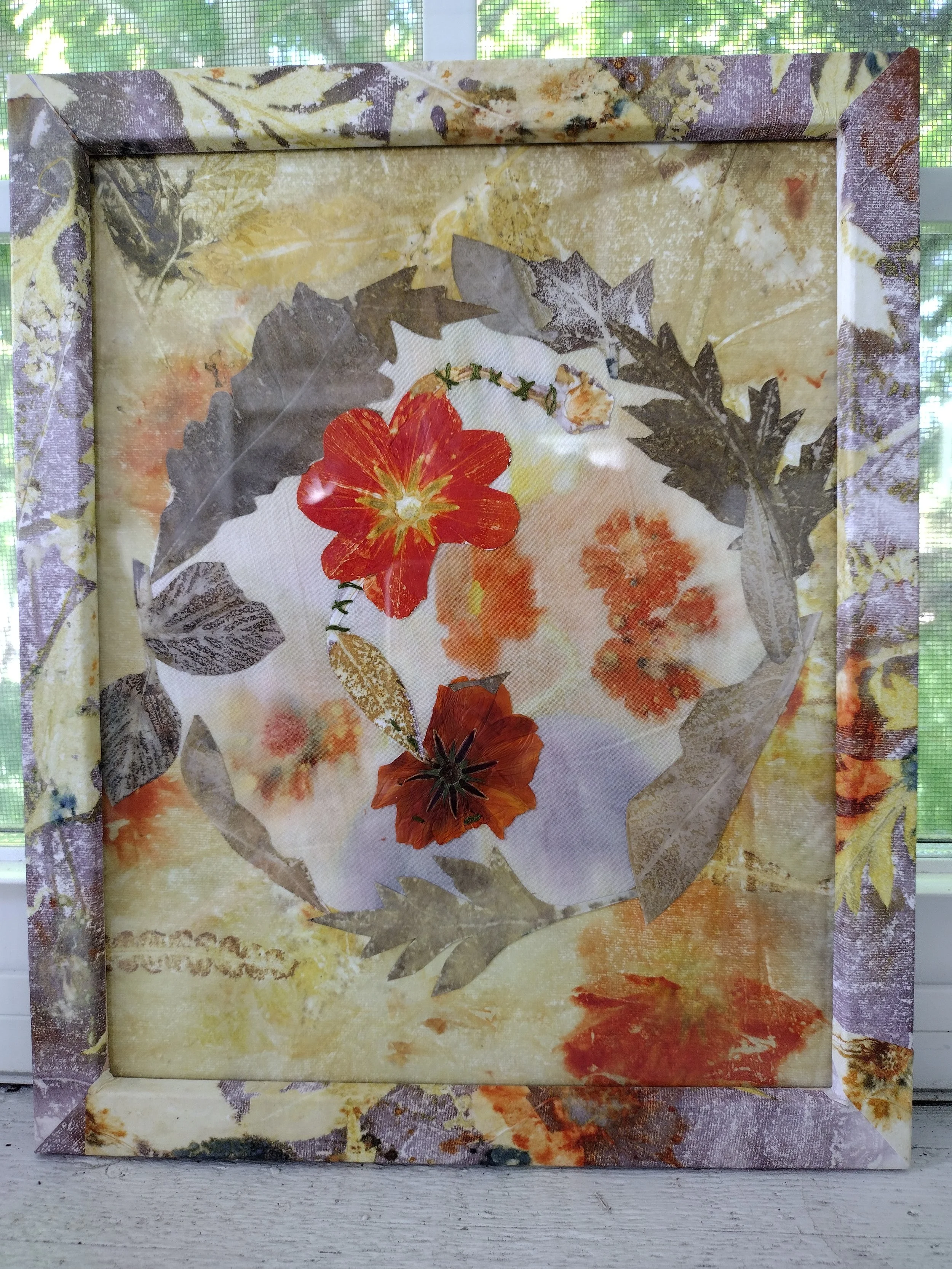 A framed artwork or collage featuring a red flower, gray leaves, and small green and beige vine-like elements, set against a colorful, textured background that includes shades of yellow, orange, and gray. By Amy Real