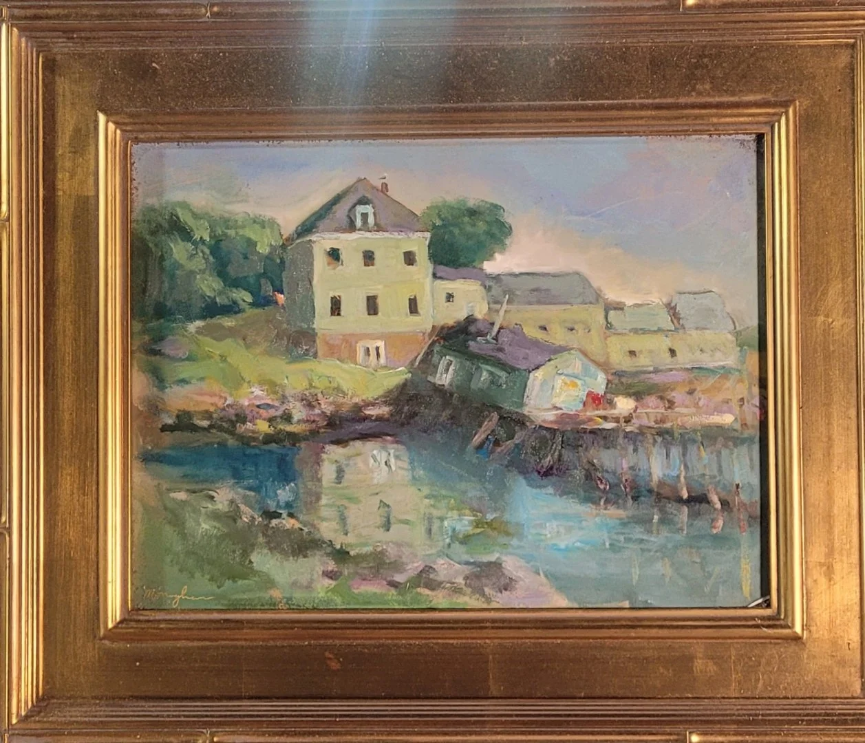 A colorful oil painting of houses by a lake, with some houses leaning and reflecting in the water, framed with a gold ornate border.