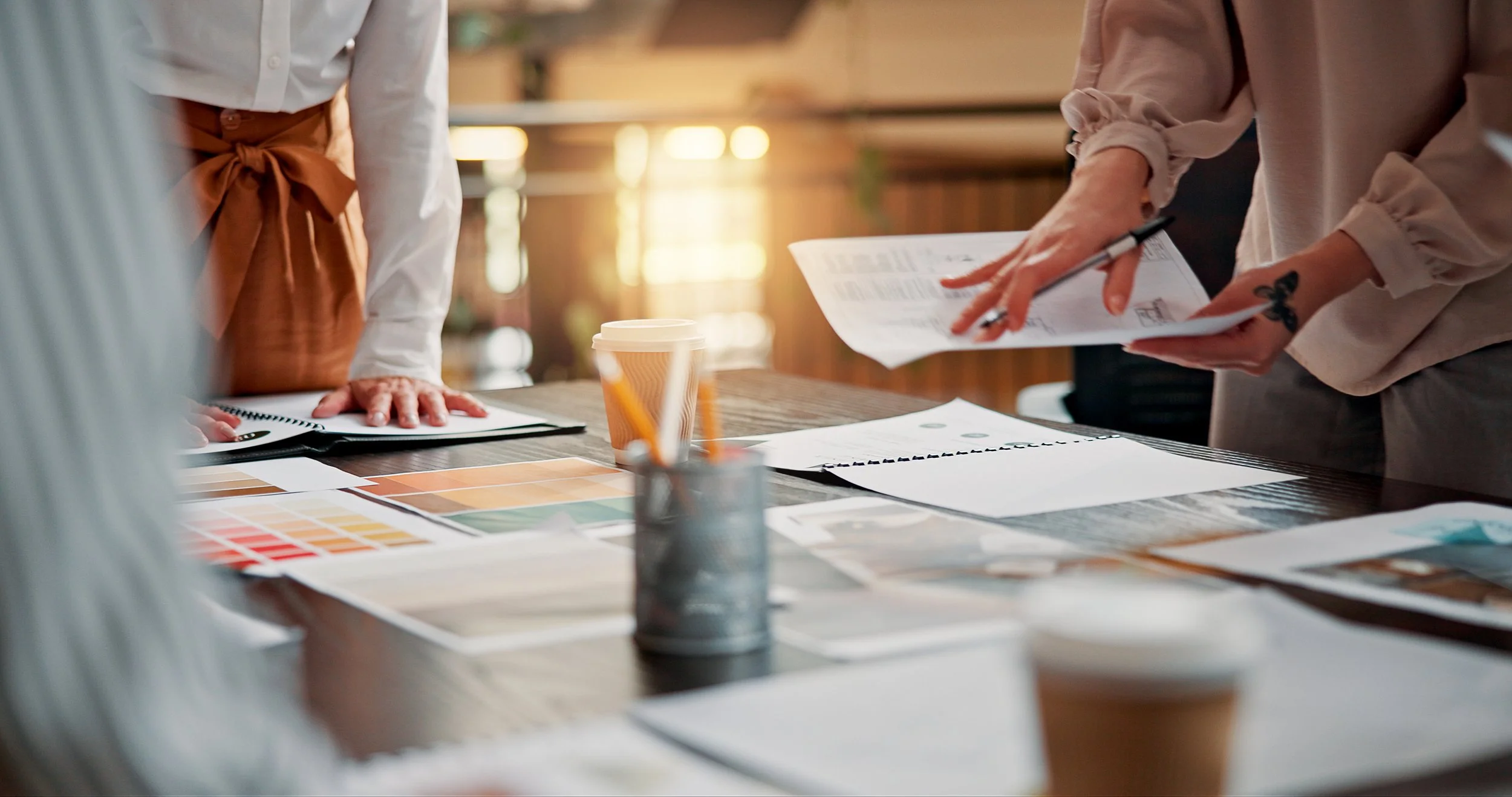 People working at a table with color swatches, documents, and a coffee cup.
