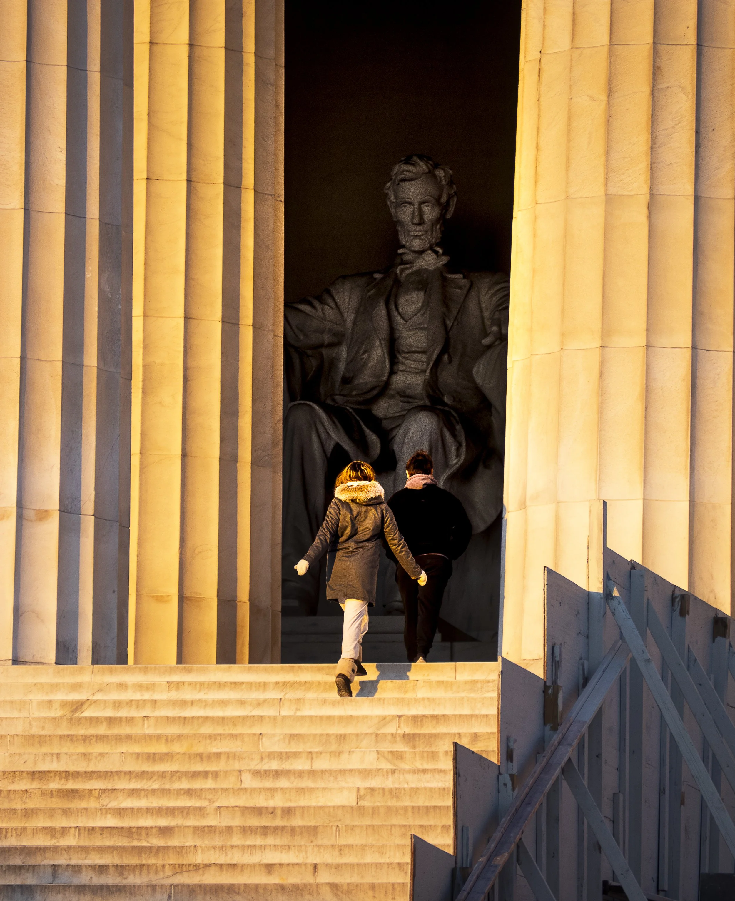 Two people ascending steps toward the Lincoln Memorial at sunset, with the giant seated Lincoln statue visible inside.