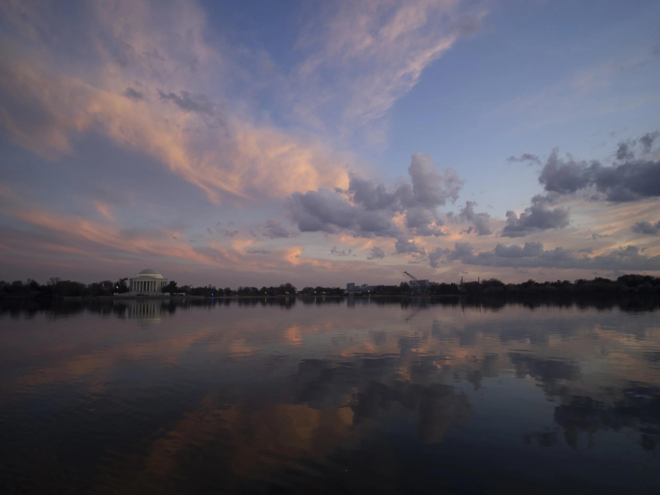 Sunset over a body of water with reflections, clouds in the sky, and a distant government building on the horizon.