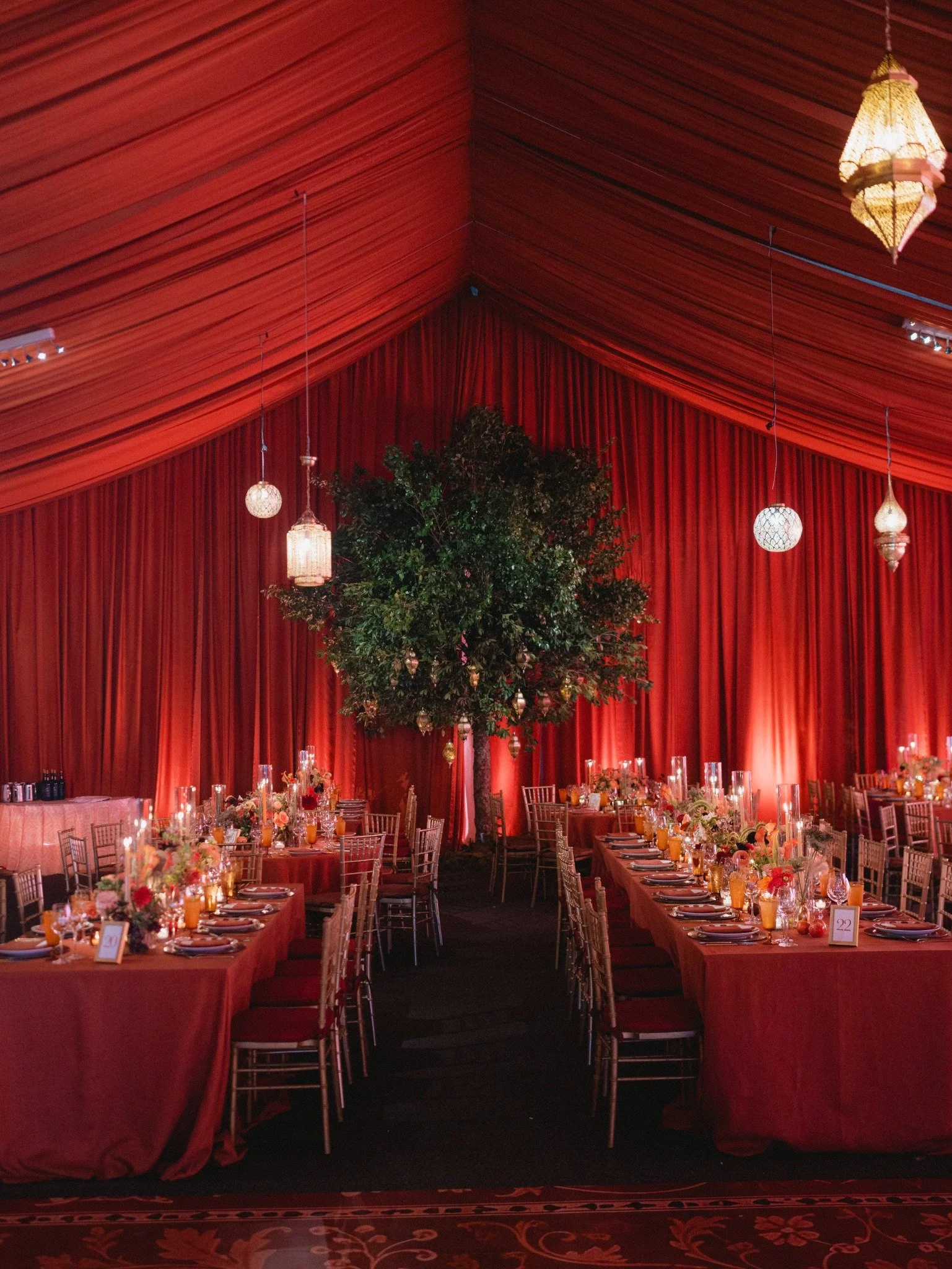 Wedding reception with red draping, hanging Moroccan lanterns and long dining tables