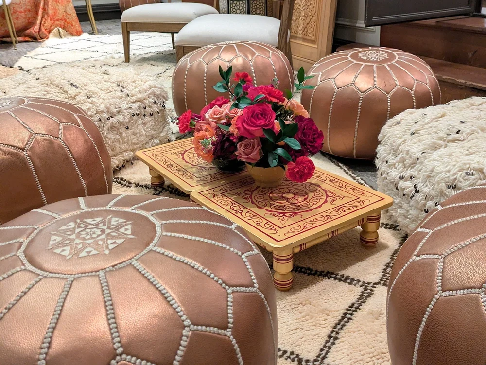 Tan leather Moroccan poufs arranged around a carved low table with flowers and layered rugs