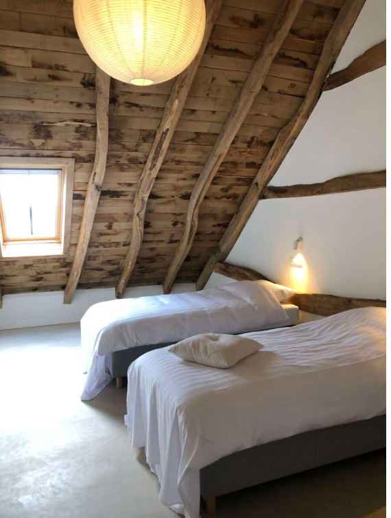 Twee bedden met witte beddengoed in een slaapkamer met een schuine houten plafond en een klein raampje.