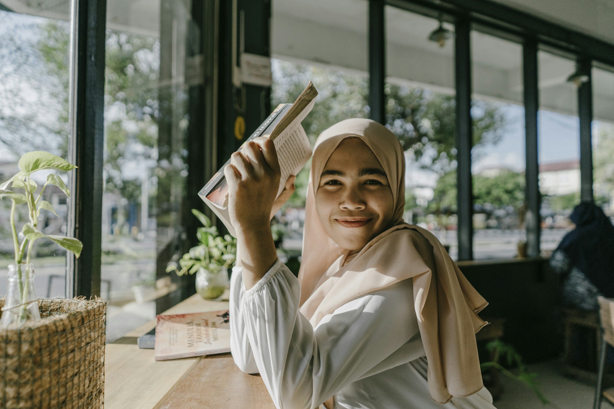 A young girl in a hijab smiling and holding a book