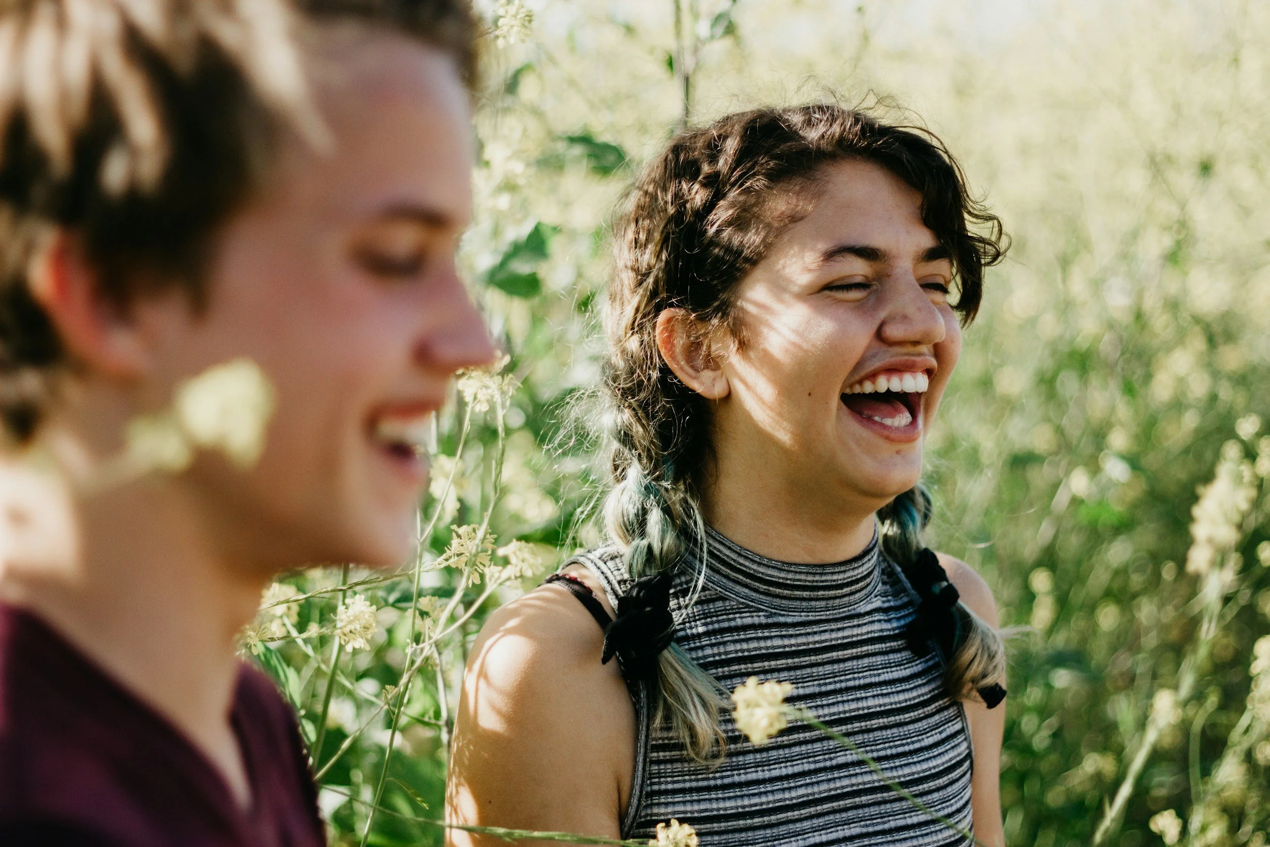 Two friends laughing together outdoors in the sunshine.