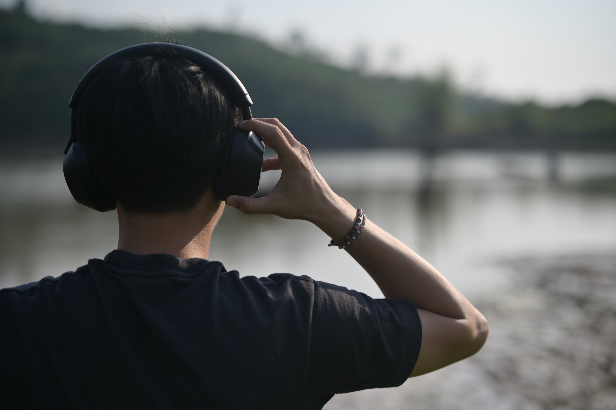 Back of a man's head, putting headphones on in front of a lake