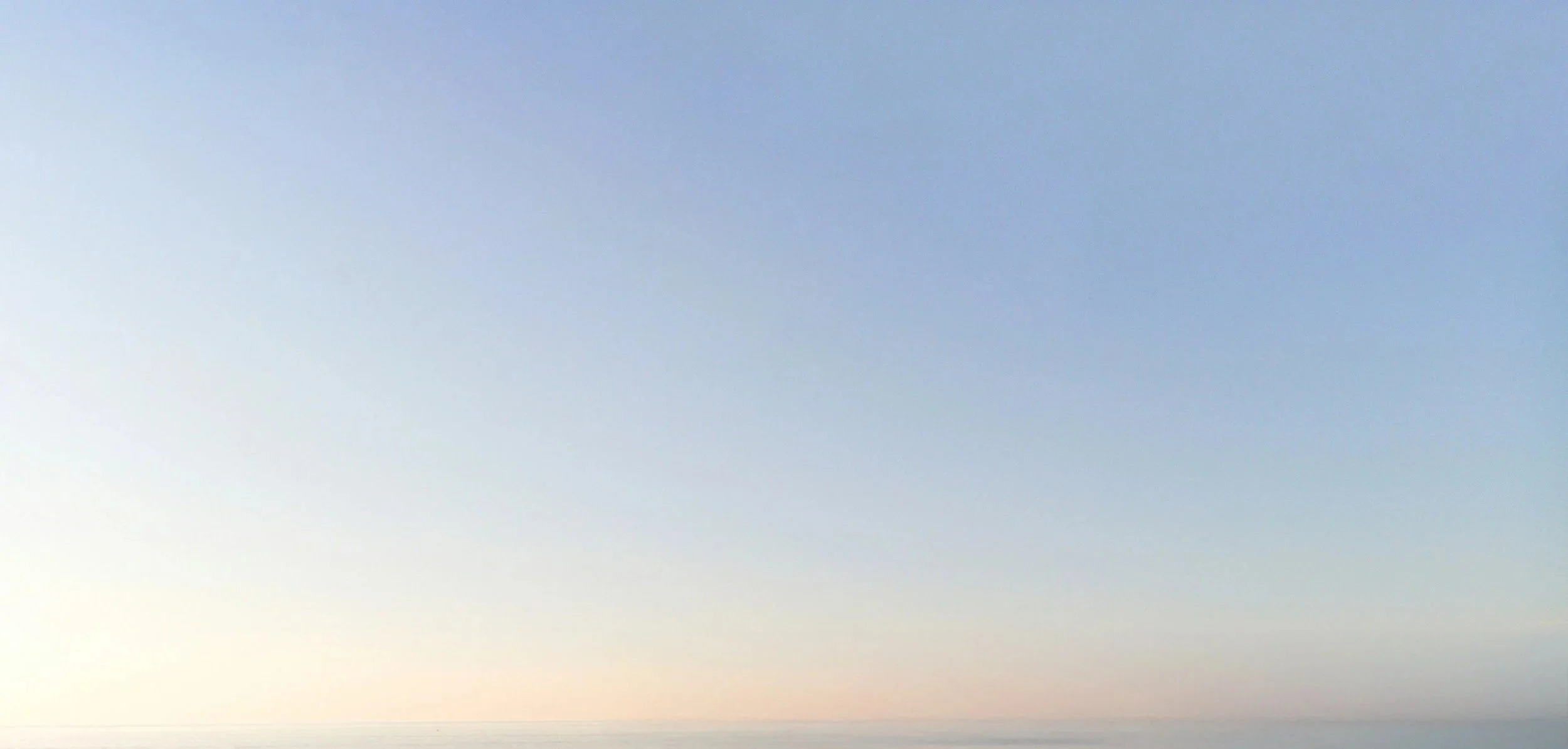A clear sky with light blue and soft pastel hues near the horizon, possibly at sunrise or sunset, over a peaceful body of water.