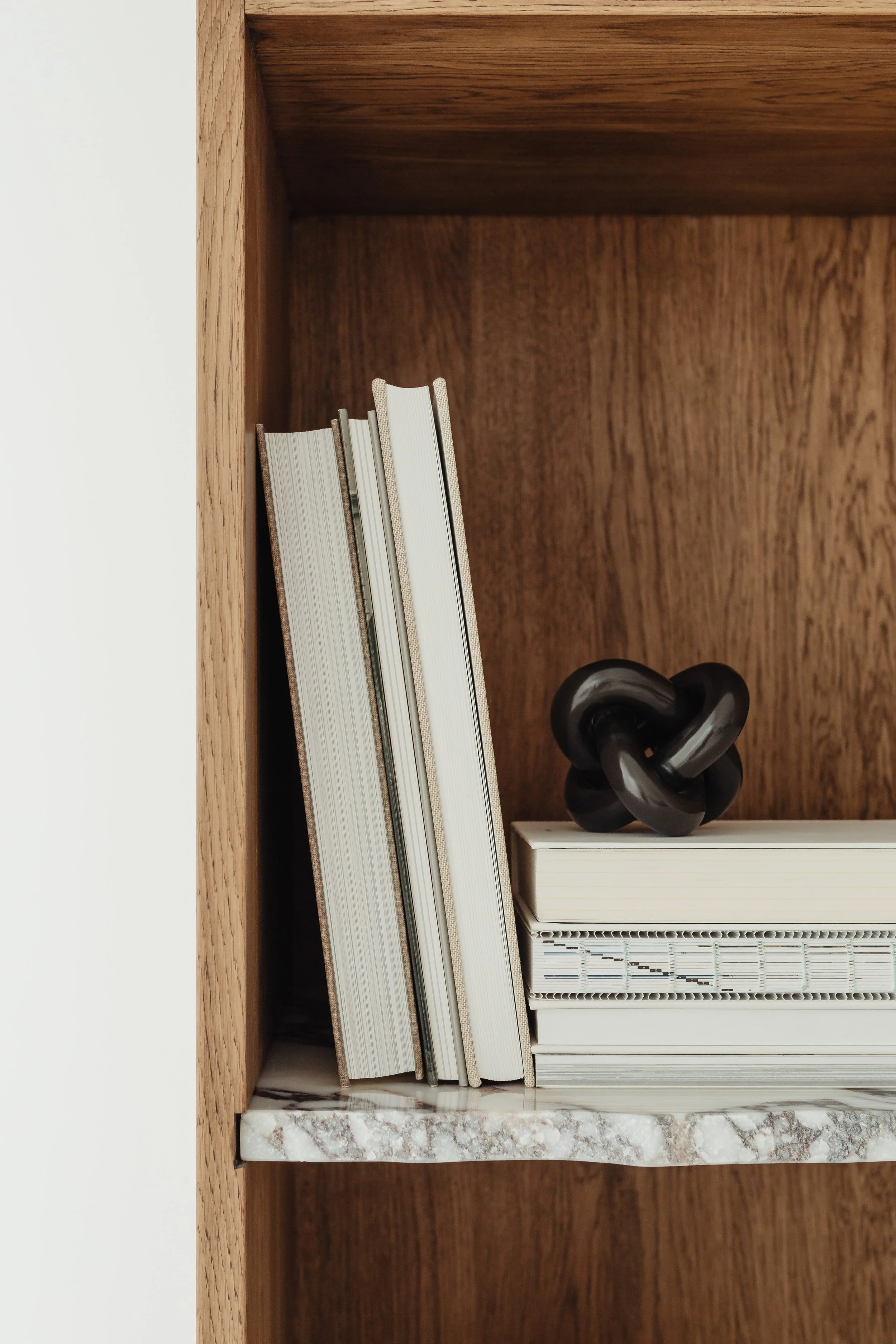 Books and decorative objects on a wooden shelf, including a knot sculpture and a white marble base.