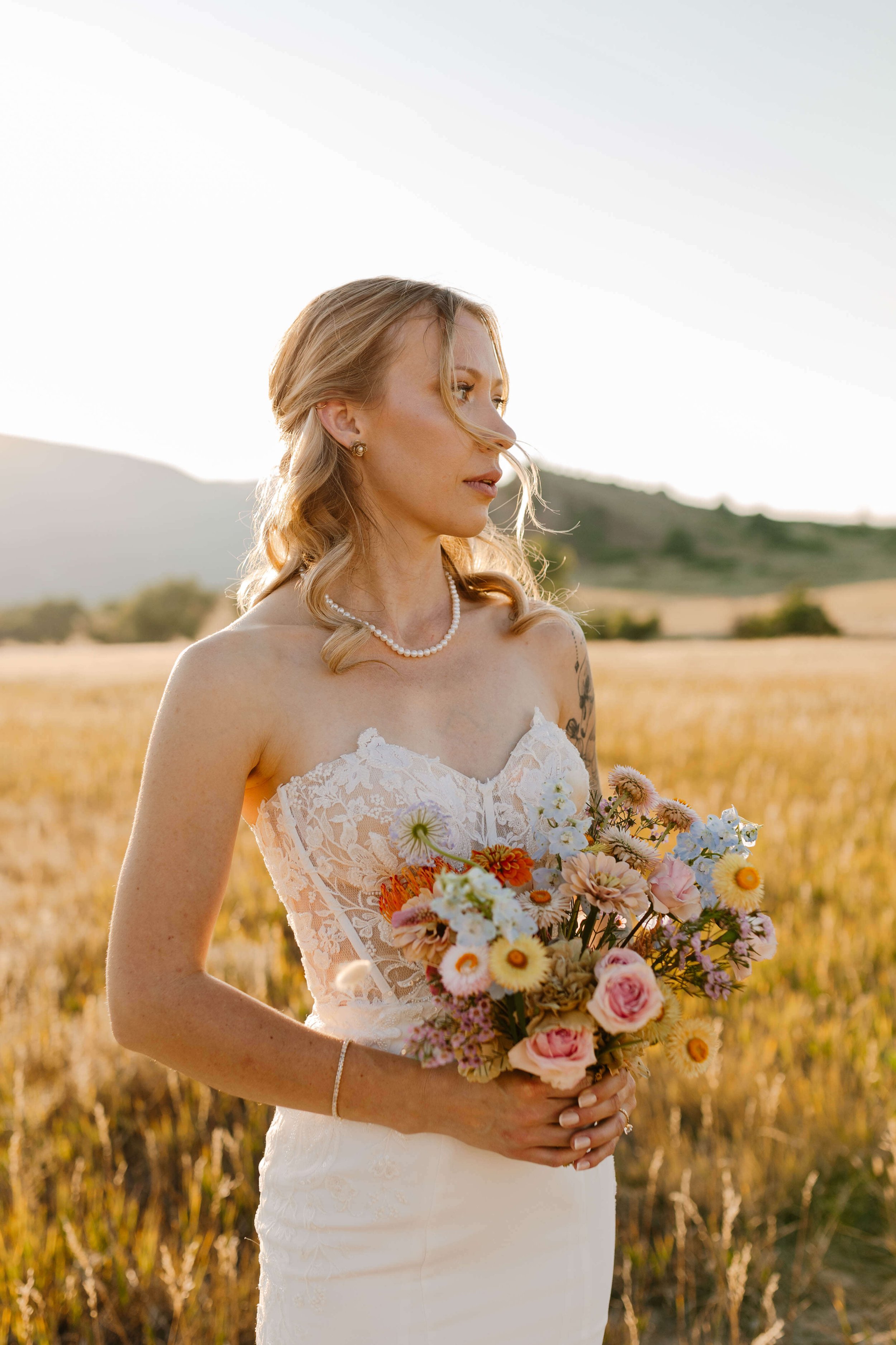 A woman in a wedding dress holding a bouquet in a field at sunset