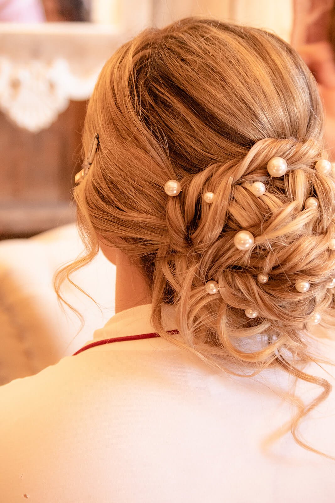 Back view of a woman's elegant blonde updo hairstyle decorated with large pearl hair accessories.