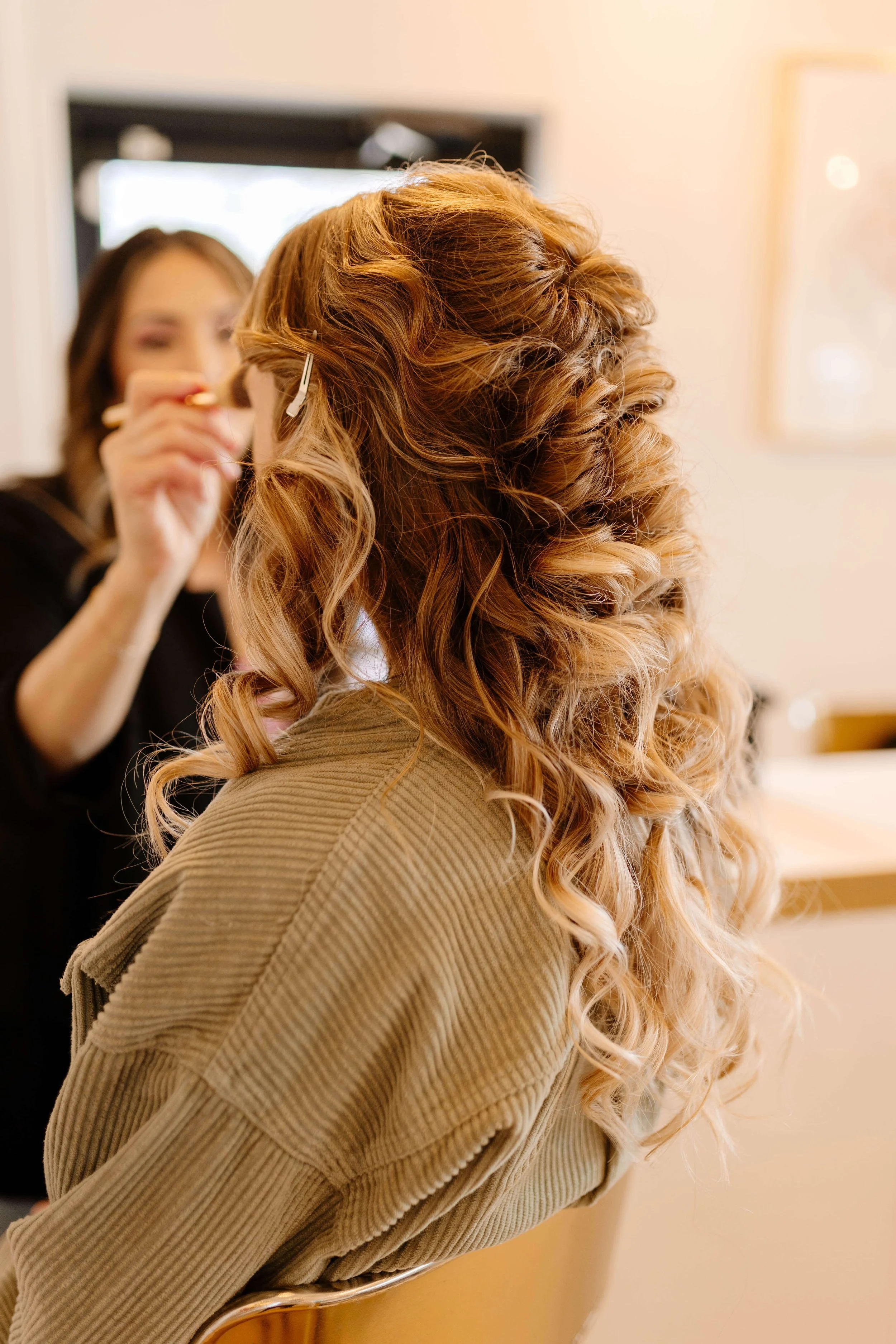 A woman with curly, blonde hair getting her hair styled by a hairstylist in a salon.