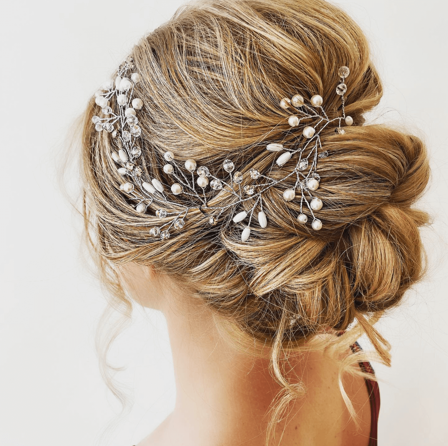 A close-up of a woman's styled blonde hair with a rhinestone and pearl hair accessory.
