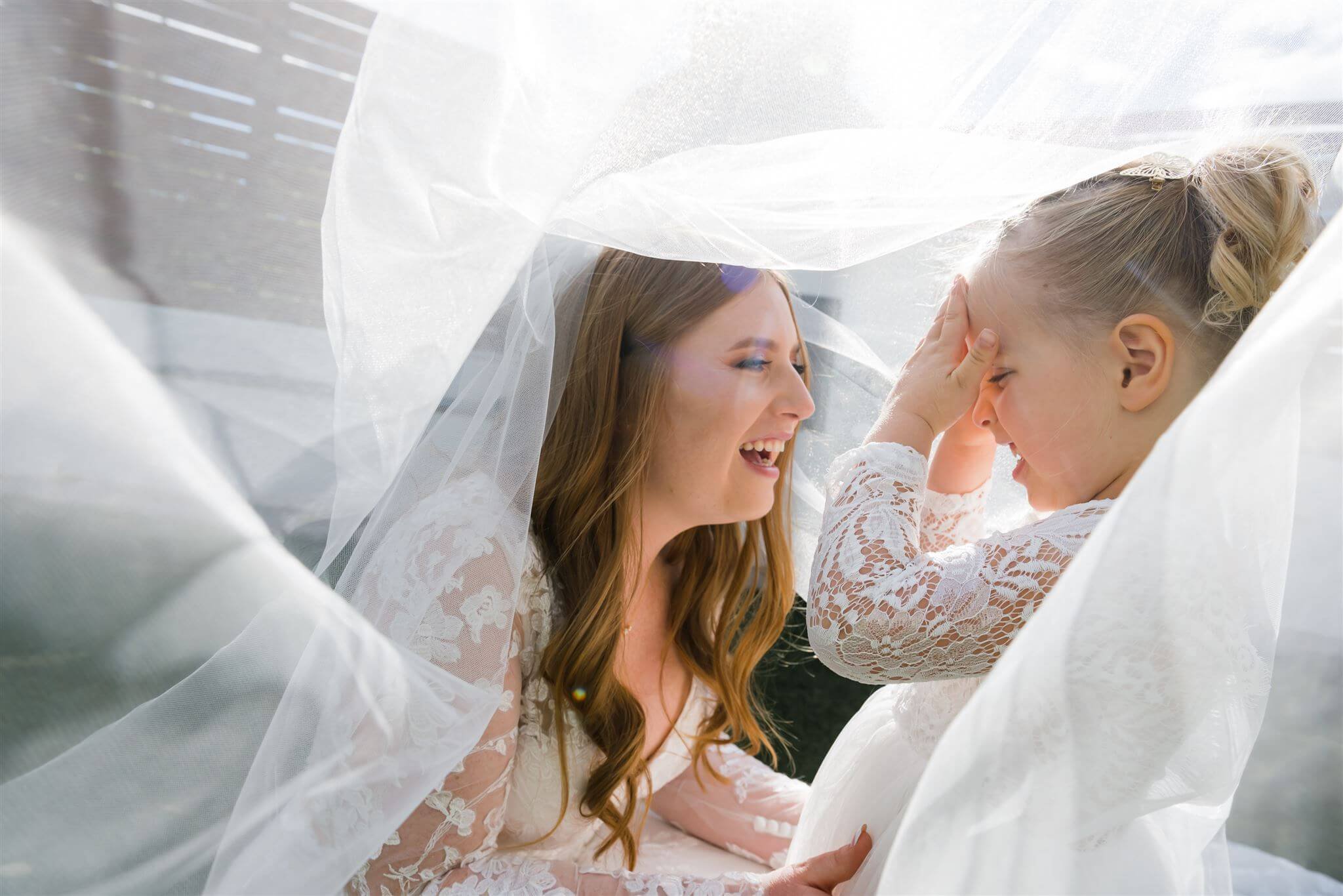 A woman and a girl sharing a joyful moment under a sheer white fabric canopy