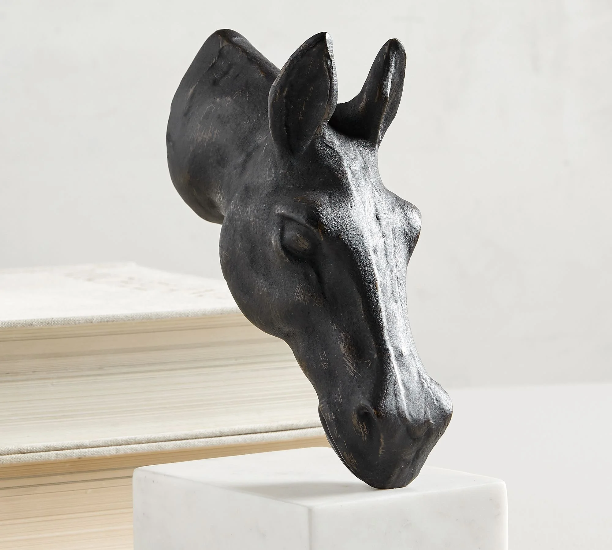 A black horse head sculpture with a textured surface on a white pedestal.