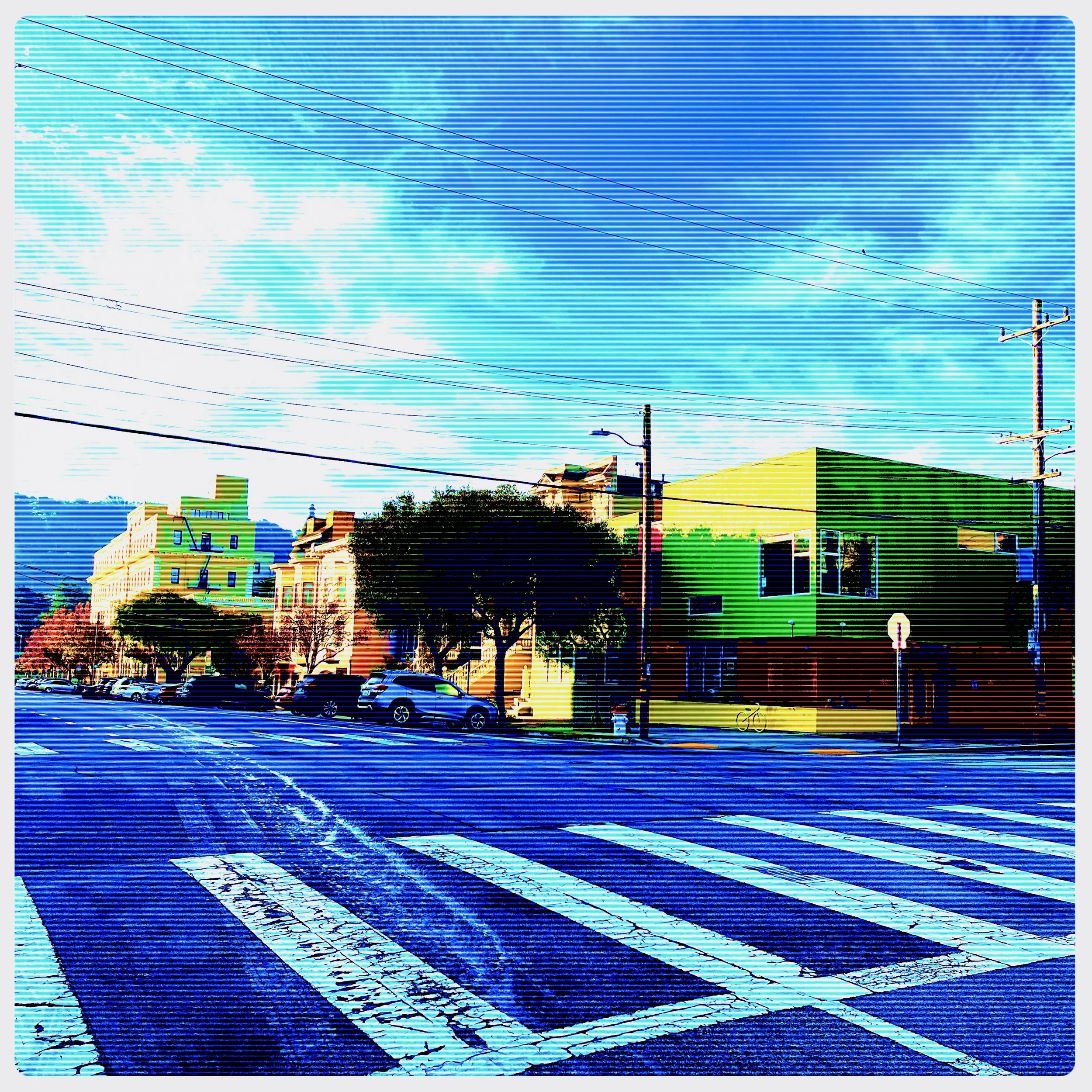 Colorful city street with crosswalk, parked cars, trees, and buildings, under a bright blue sky with clouds.