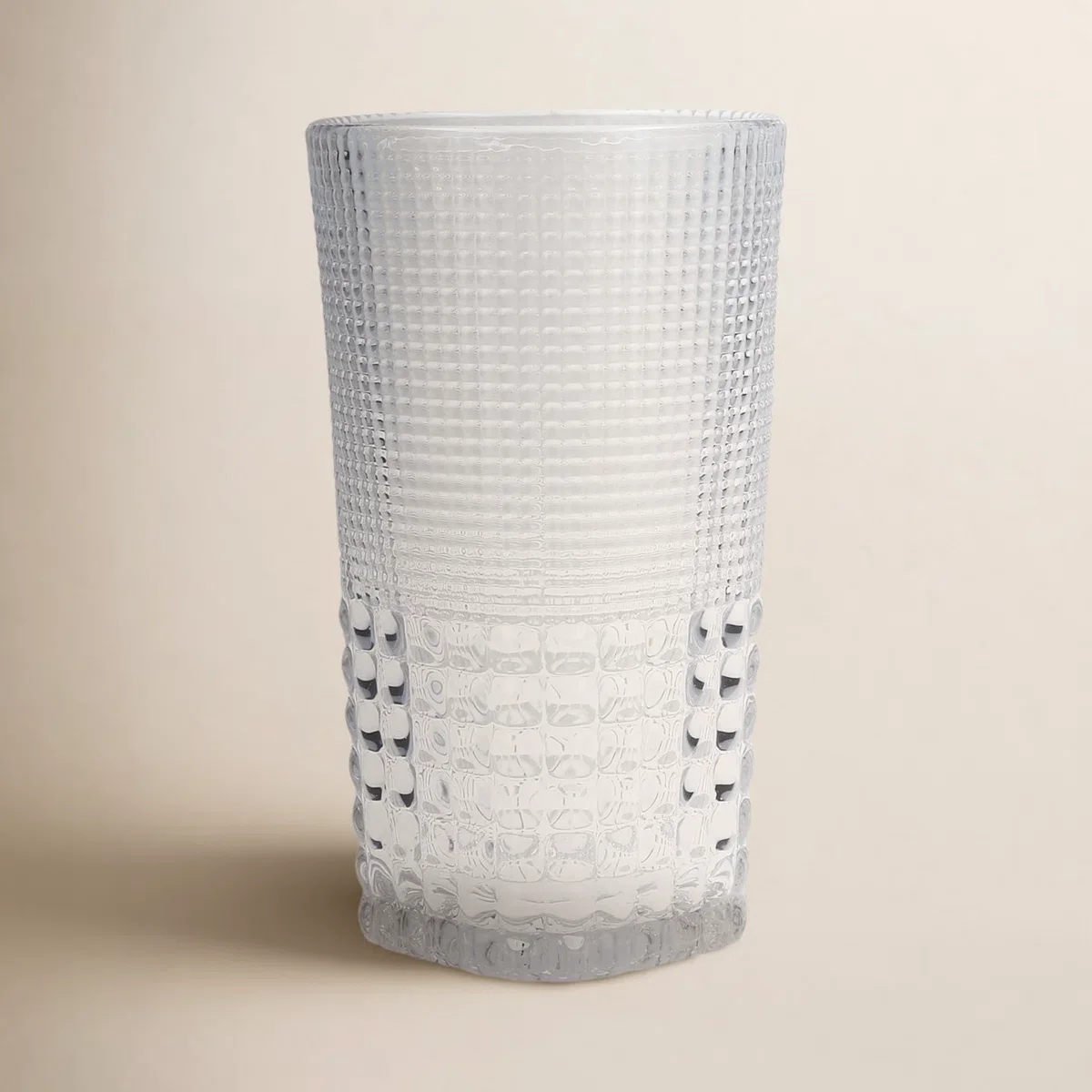 A tall, transparent glass tumbler with a textured, grid-like surface design.