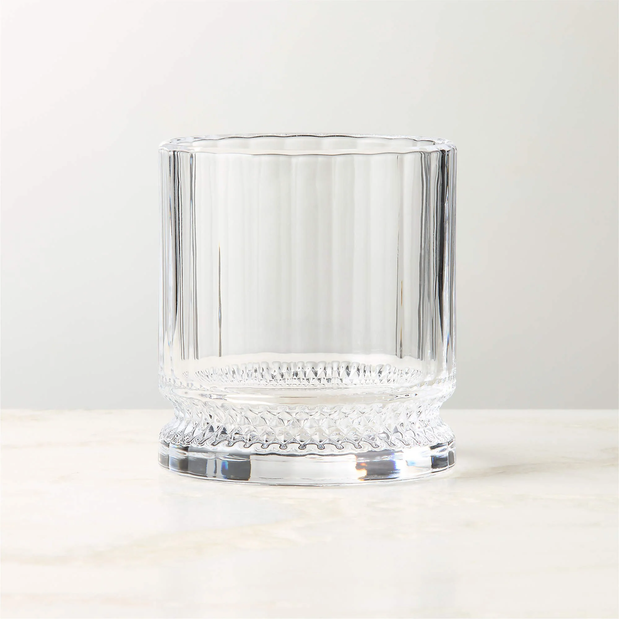 Empty clear glass tumbler with decorative pattern on the base, set on a light surface against a neutral background.