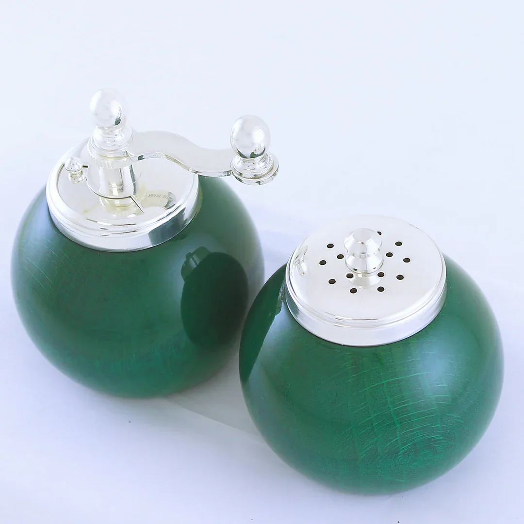 Green vintage salt and pepper shakers with transparent plastic tops, one with a turnstile for dispensing salt, the other with holes for pepper, placed on a white surface.
