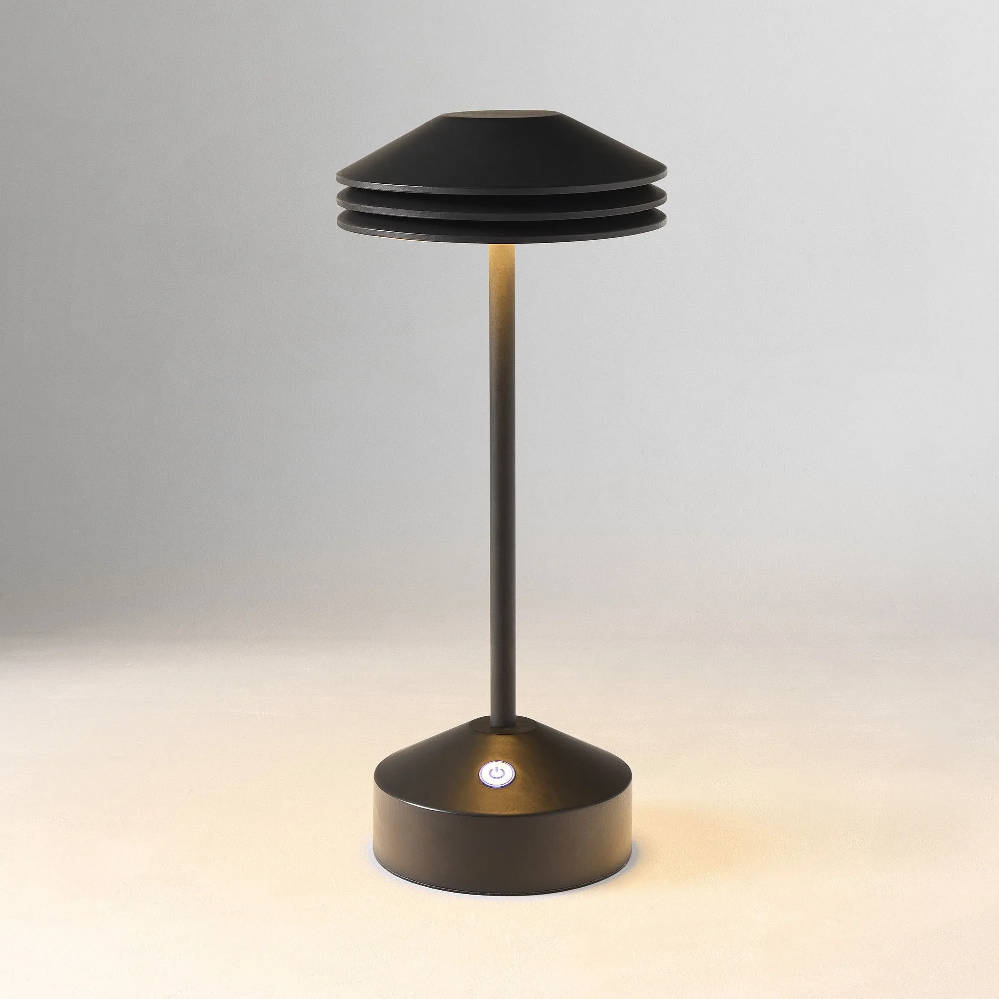 cordless Black table lamp with layered lampshade and control button on a plain surface.