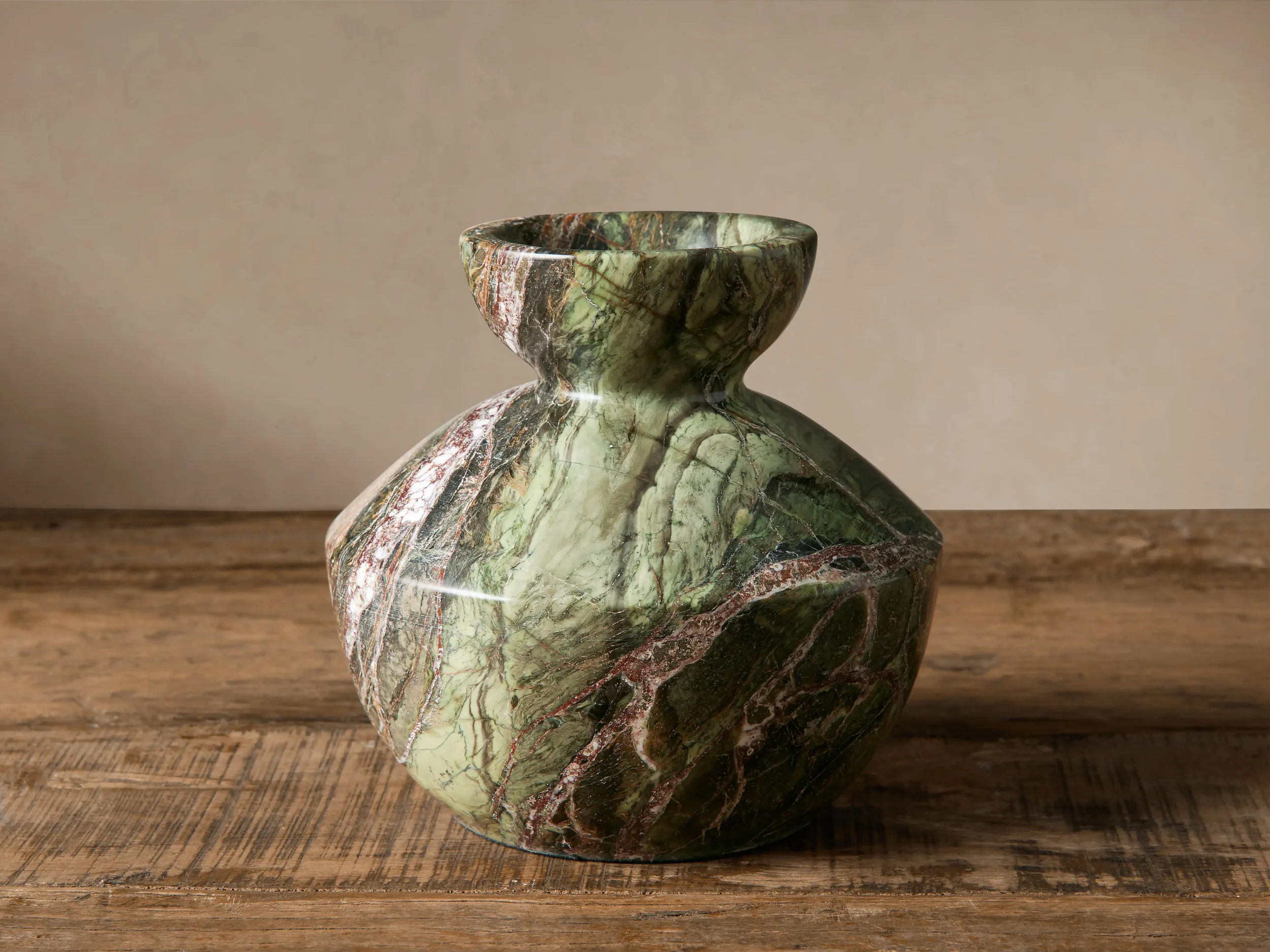 A green and brown marble vase with a narrow neck placed on a wooden surface against a plain beige background. interior decor, classic