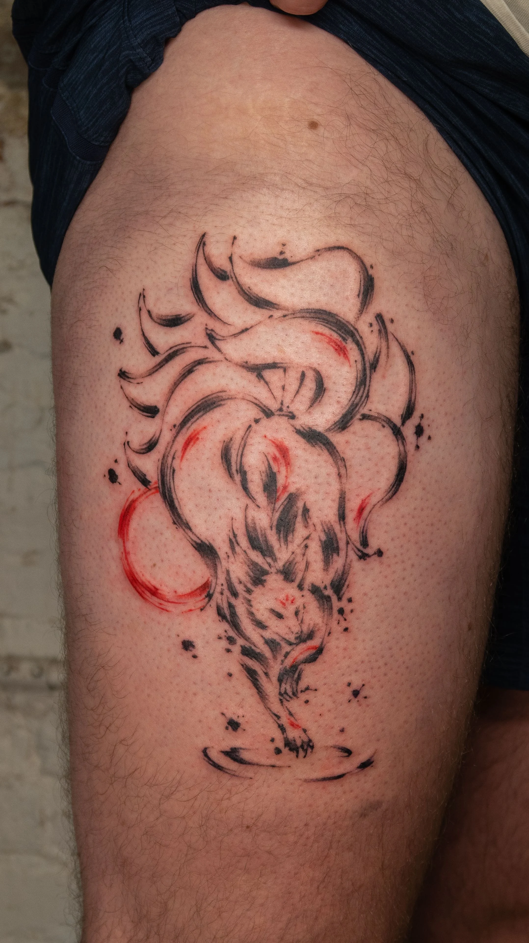 Tattoo of a howling wolf with flames and abstract ink splashes on the upper arm.