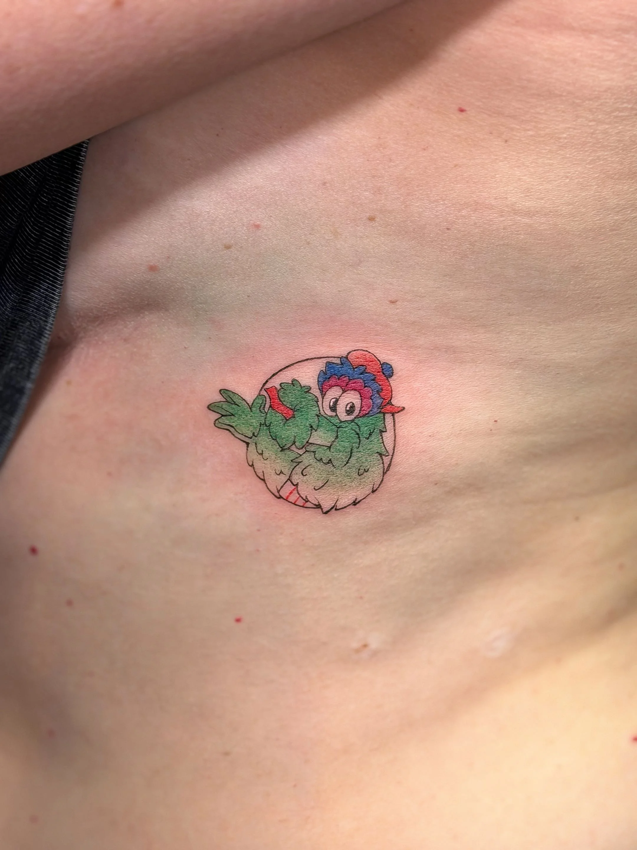 Close-up of a person's upper chest with a colorful tattoo of a cartoonish creature and small red spots.