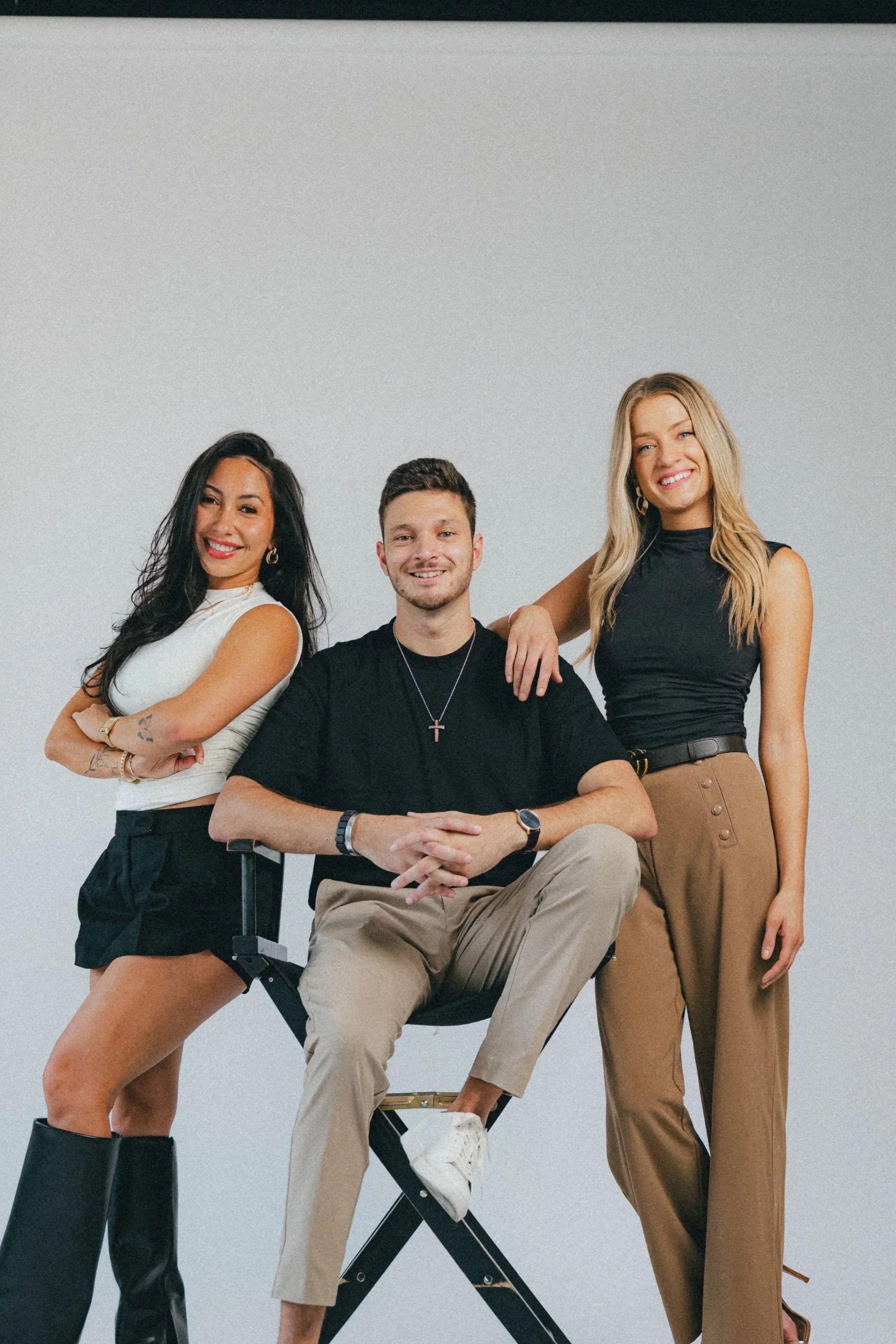 Three people posing together, two women and one man, smiling against a plain background.