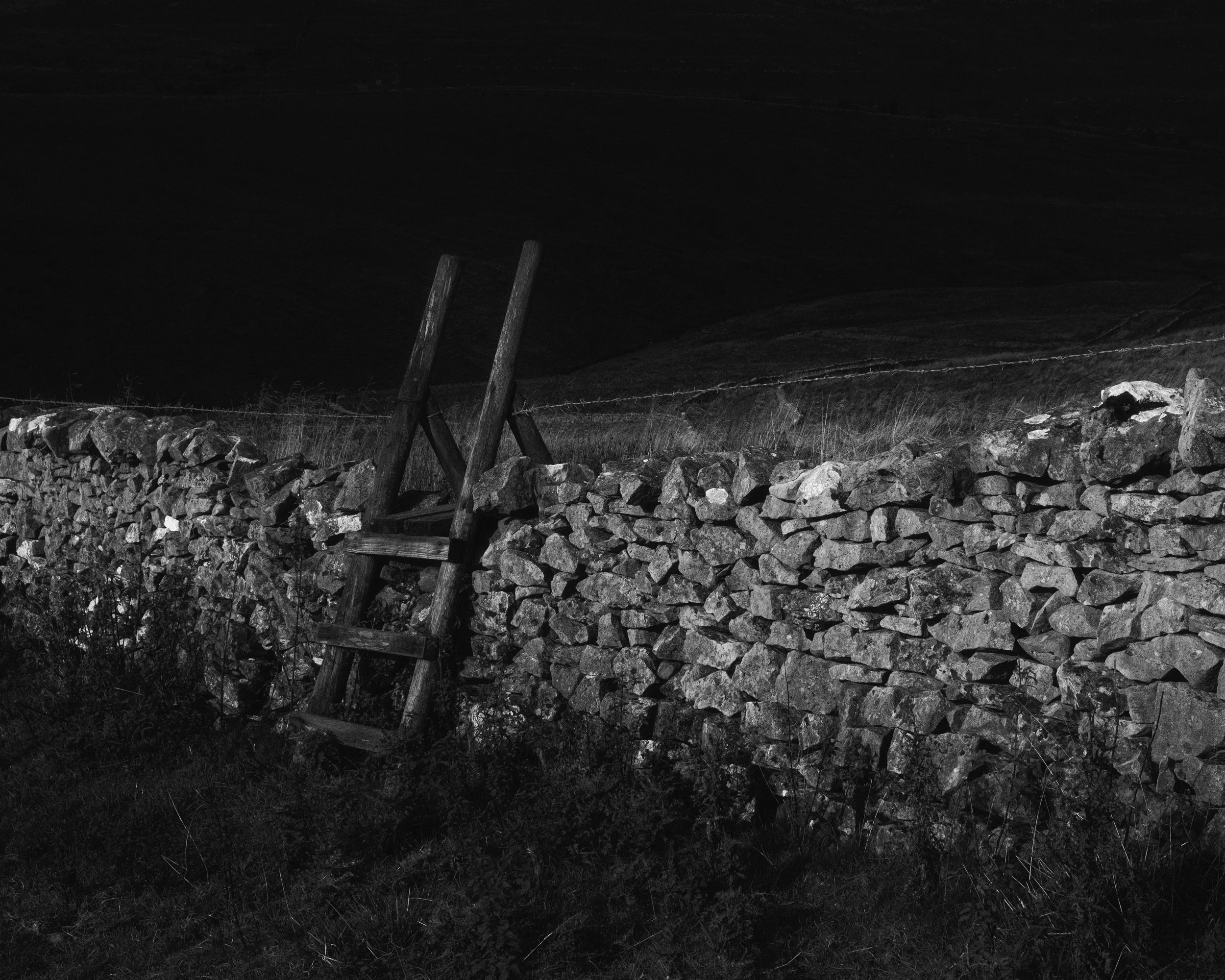 Wooden stile over a dry stone wall, shadow covered landscape in the background