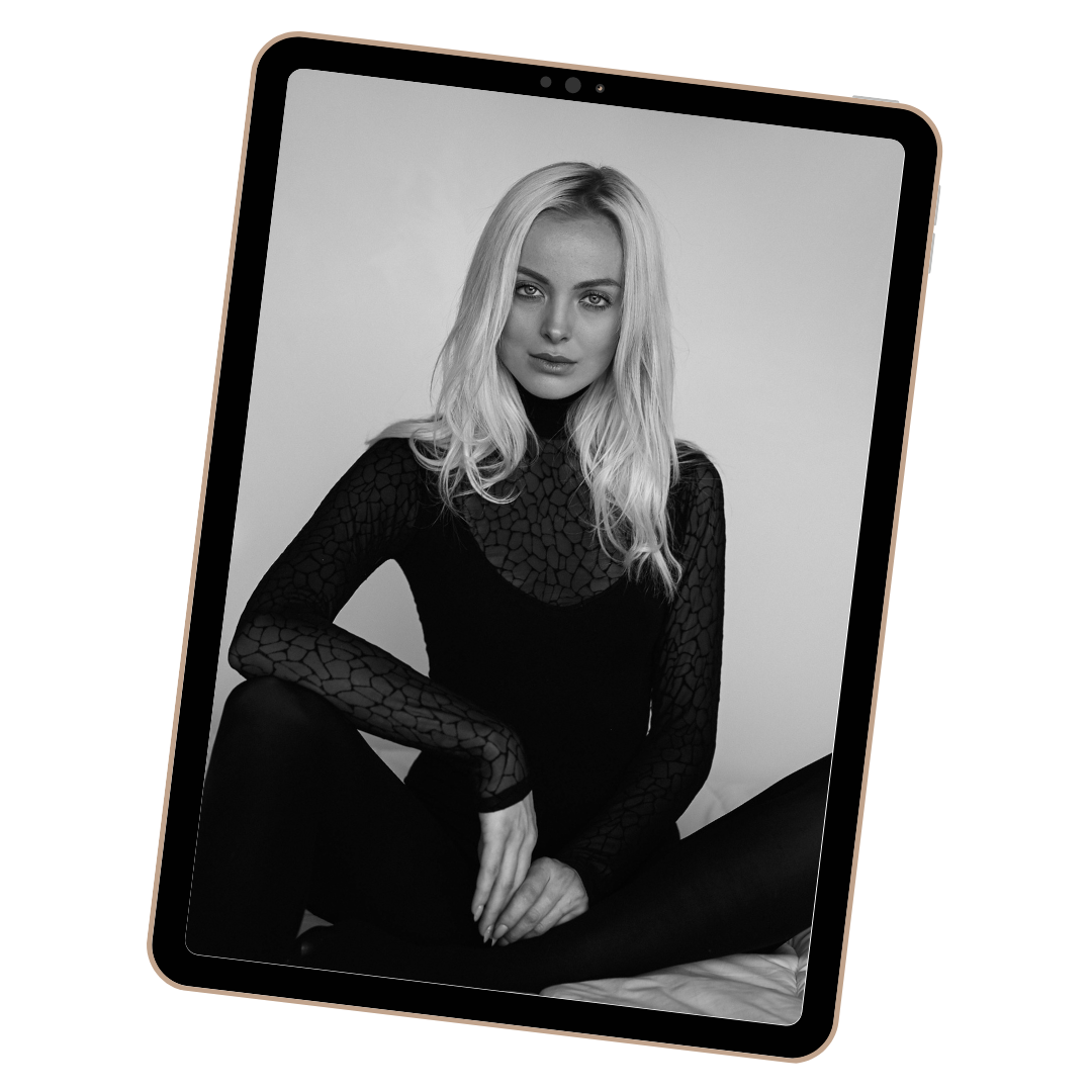 Black and white photo of a young woman with long, blonde hair wearing a dark, patterned long-sleeve top, sitting against a plain background