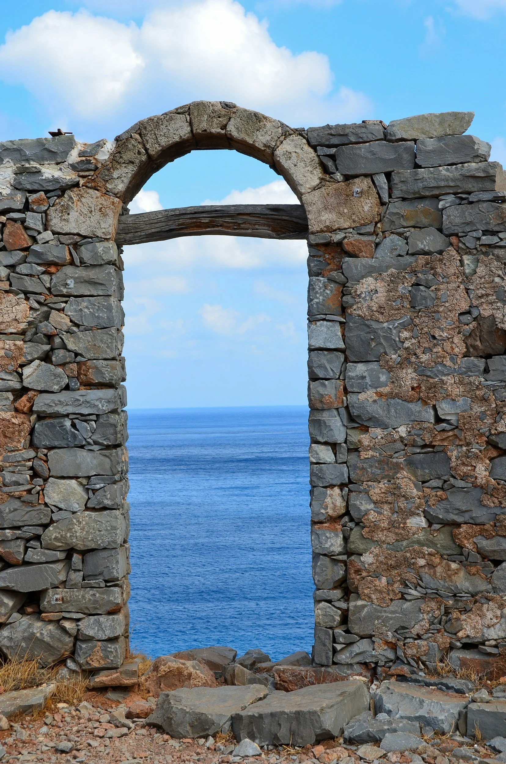 Stone window frame with an arch, overlooking the ocean with a partly cloudy sky.