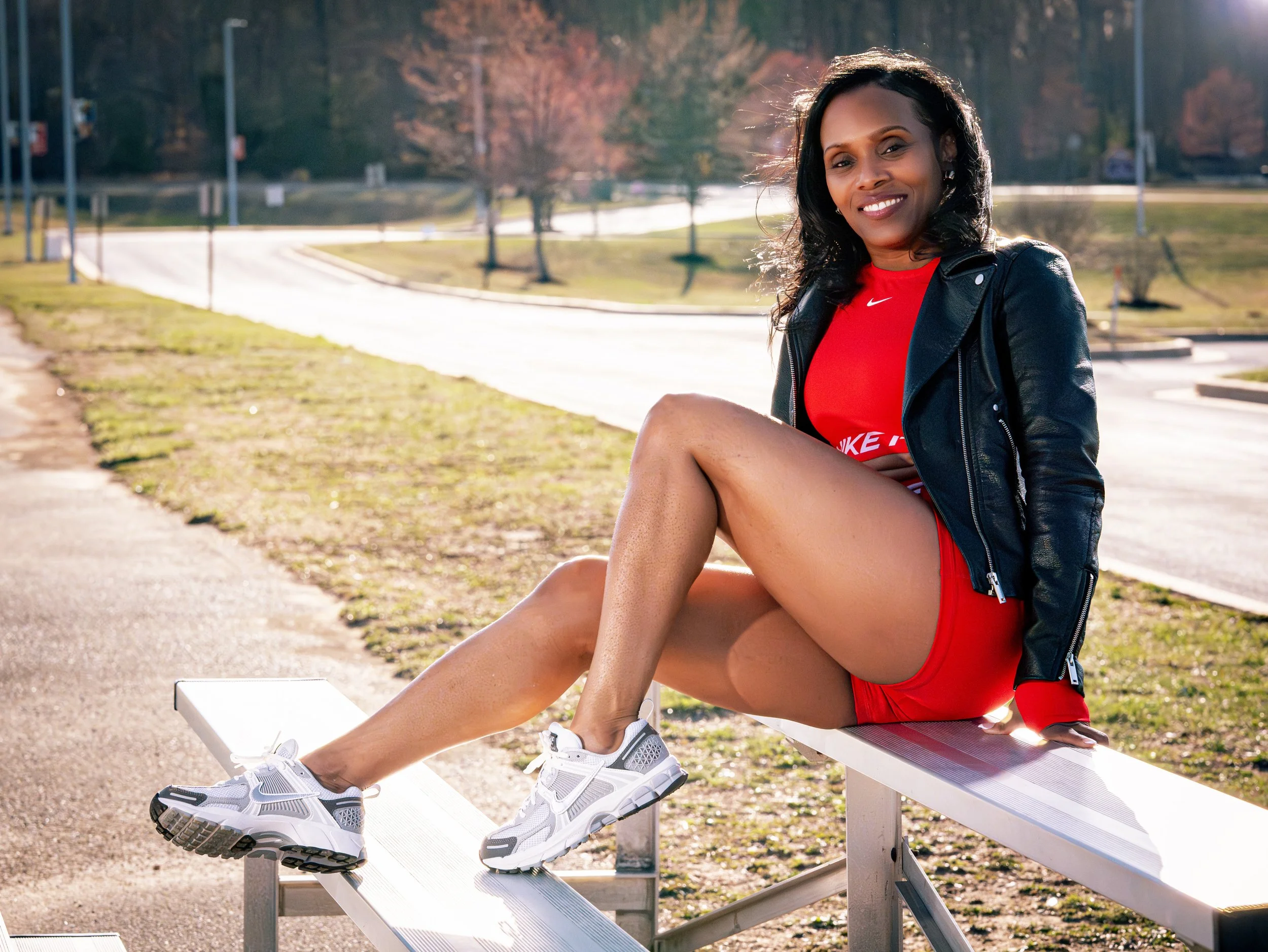 Woman sitting on outdoor bench wearing red athletic outfit and black jacket