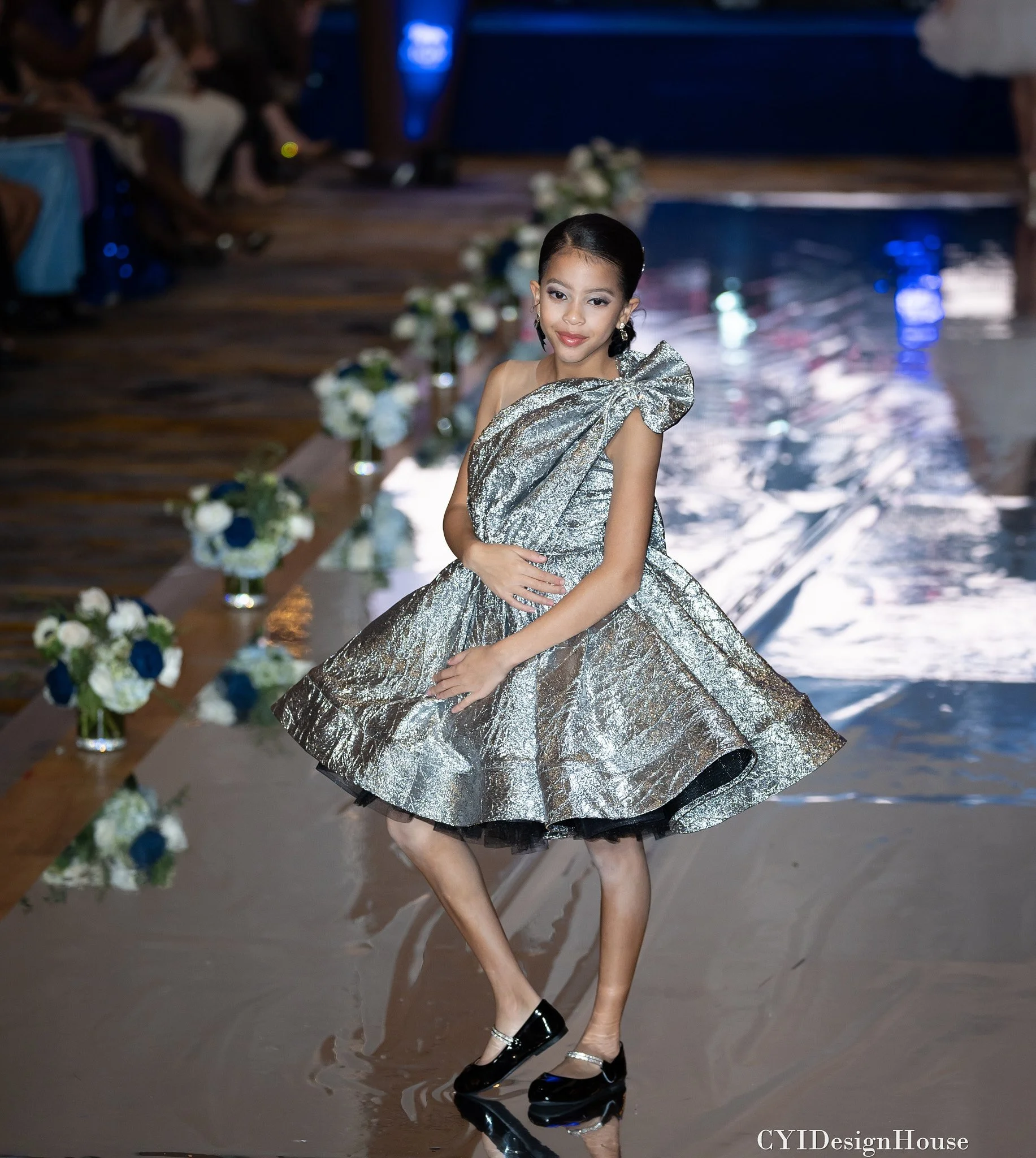 Young model in silver dress on runway with floral decorations