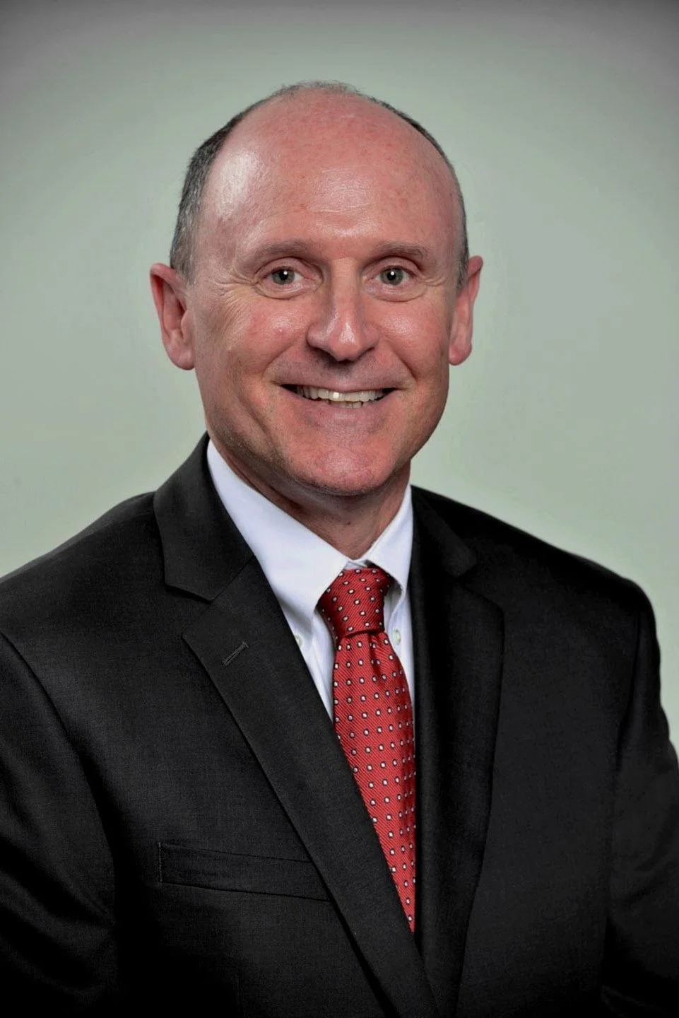 Smiling man in a suit with a red tie against a neutral background.