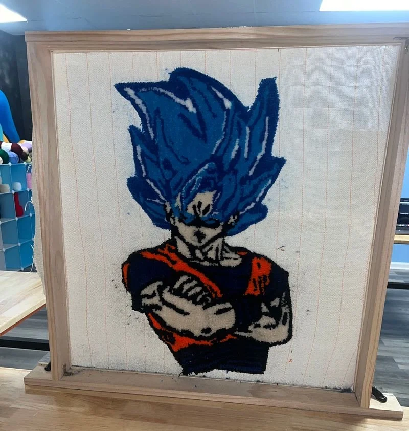 Cross-stitch artwork of Goku from Dragon Ball Z with blue hair, wearing an orange and black outfit, arms crossed.