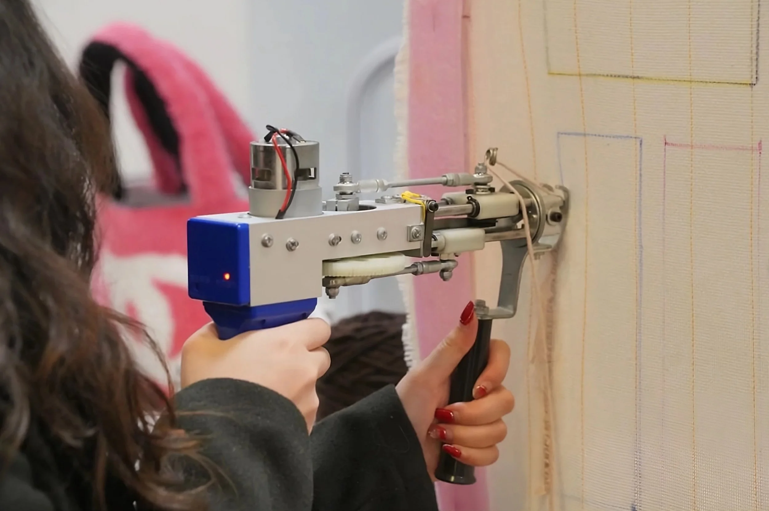 Person stitching a fabric with a mechanical stitching gun on a wall.