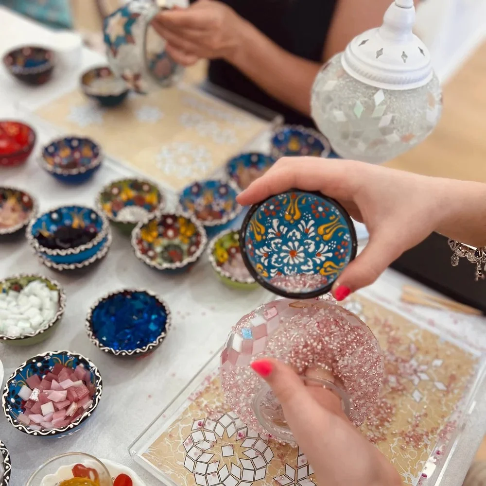 People creating mosaics with colorful tiles and patterned bowls.