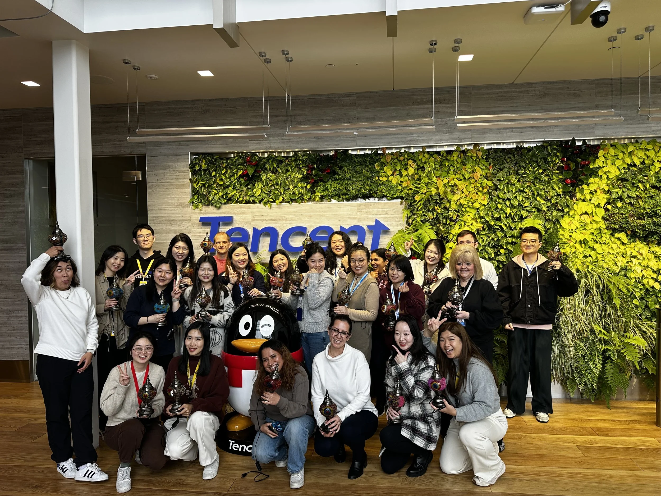 Group of people posing with a penguin statue inside a Tencent office, standing in front of a green wall featuring the Tencent logo.
