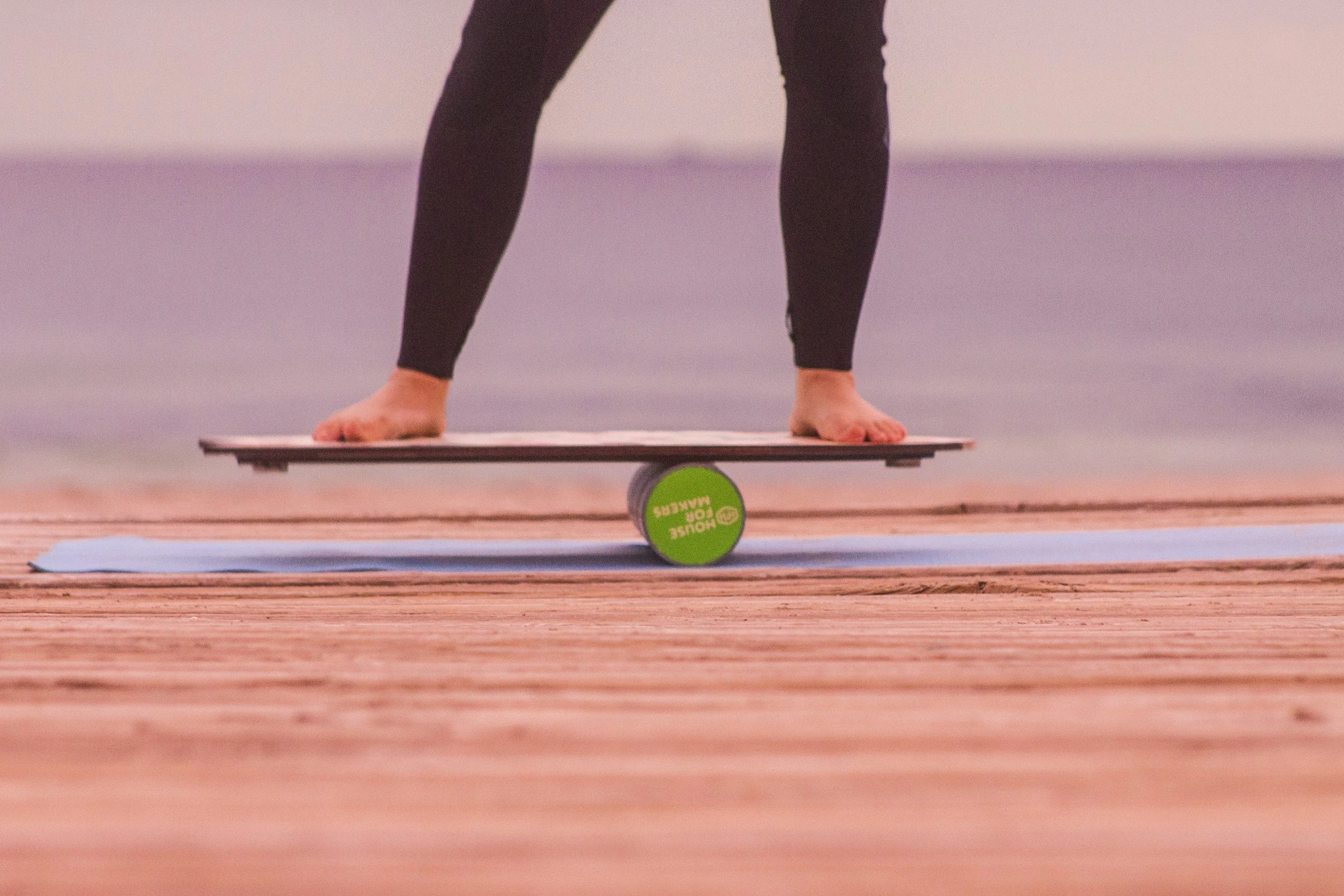 Person balancing on balance board with roller, wearing black leggings, near ocean