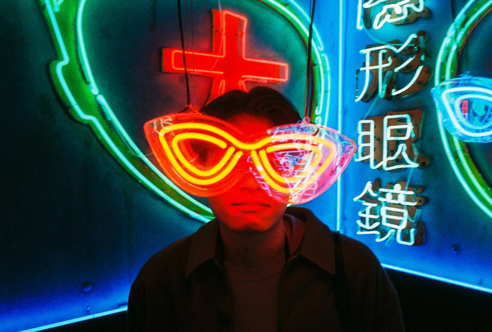 Person framed by a glowing neon eyewear sign outside a Hong Kong optician at night