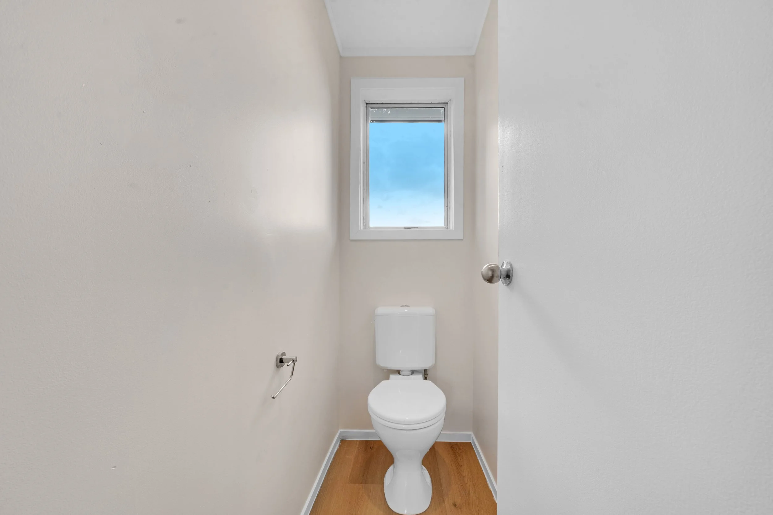 Small bathroom with toilet, window above, and hardwood floor.