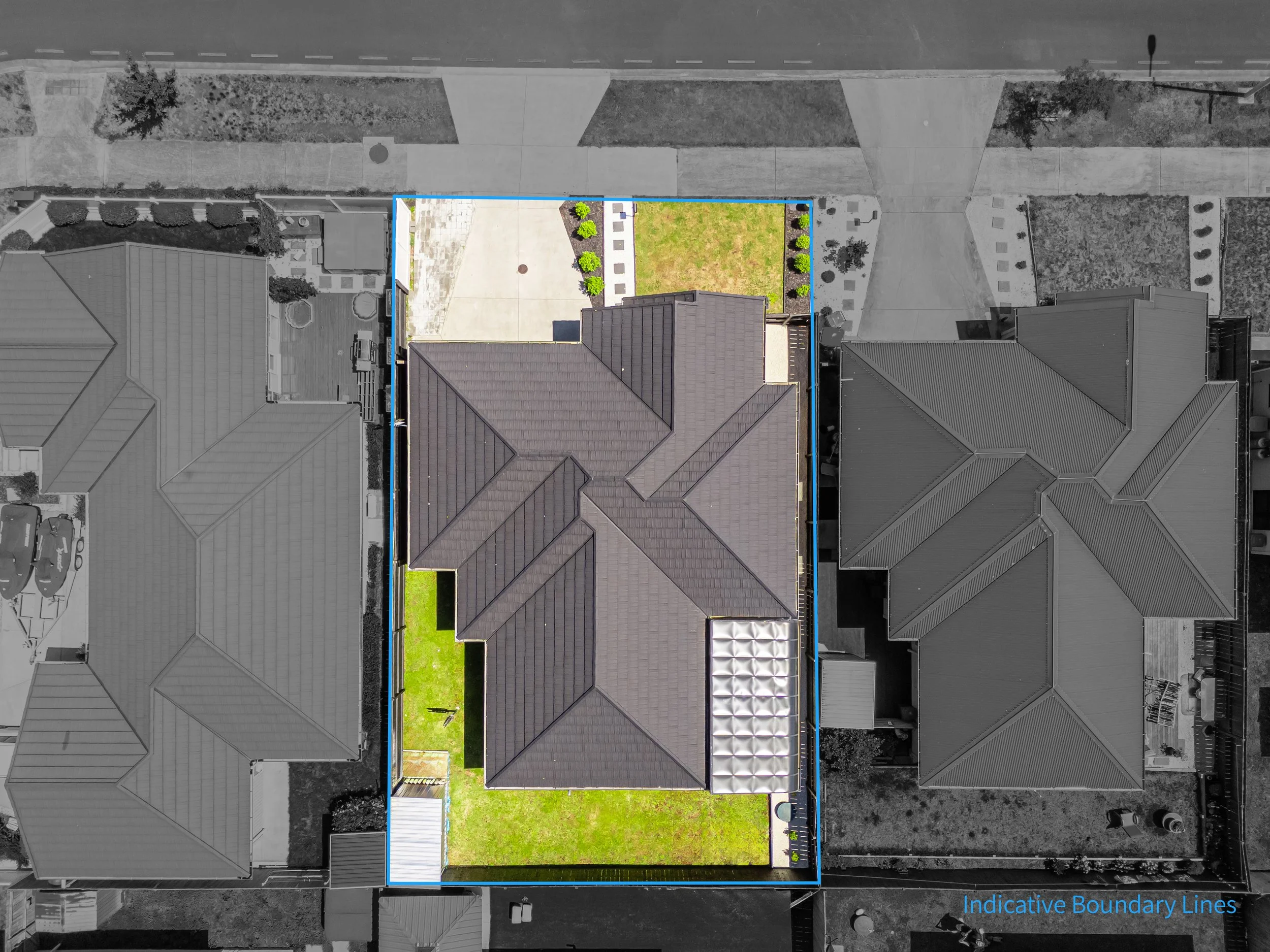 Aerial view of a house with a gray roof, surrounded by neighboring houses, with a front street above and a backyard enclosed by fencing, featuring a lawn, patio, and small garden area.