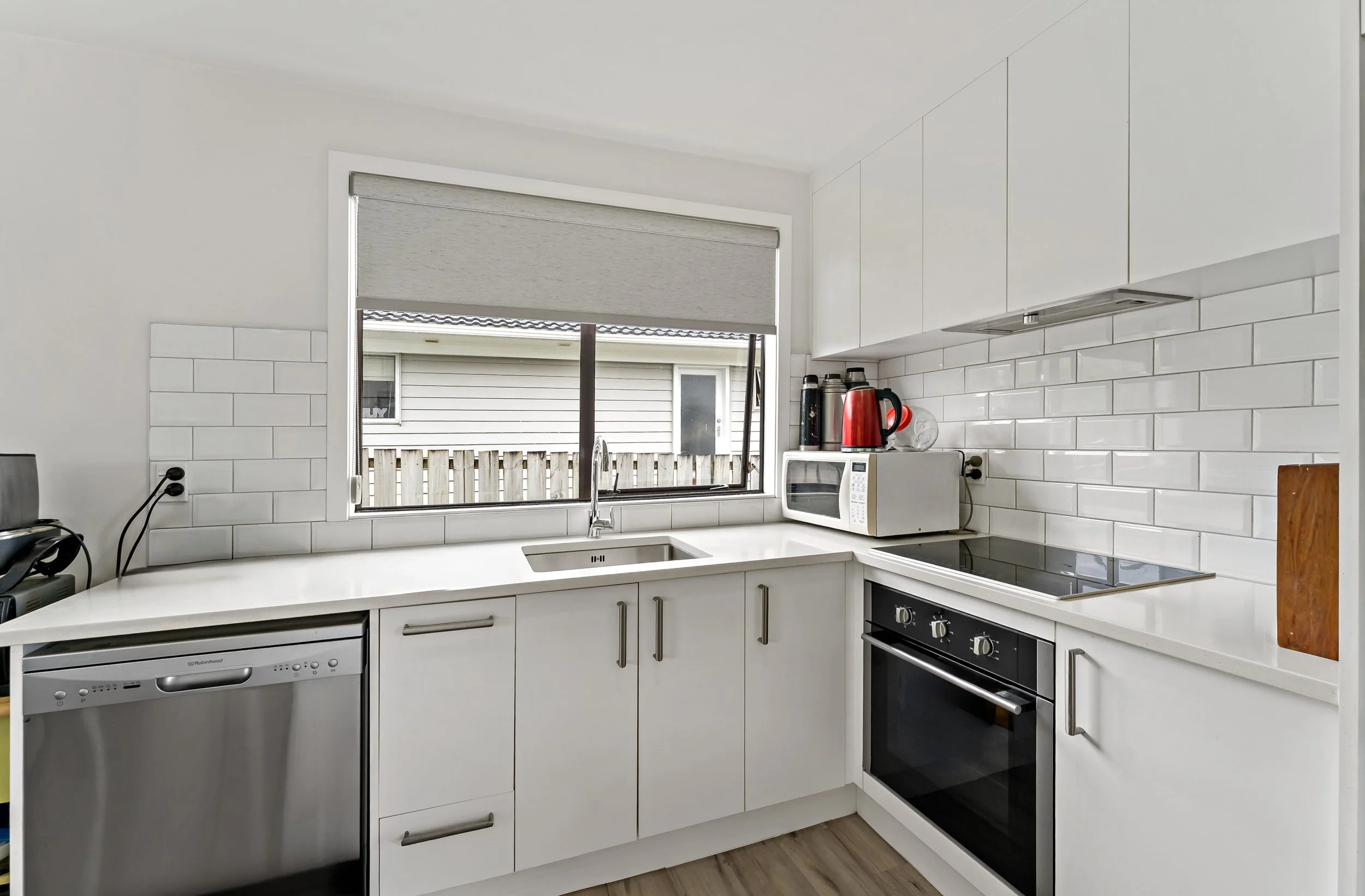 Modern white kitchen with window, white cabinets, and black oven, microwave, and dishwasher.
