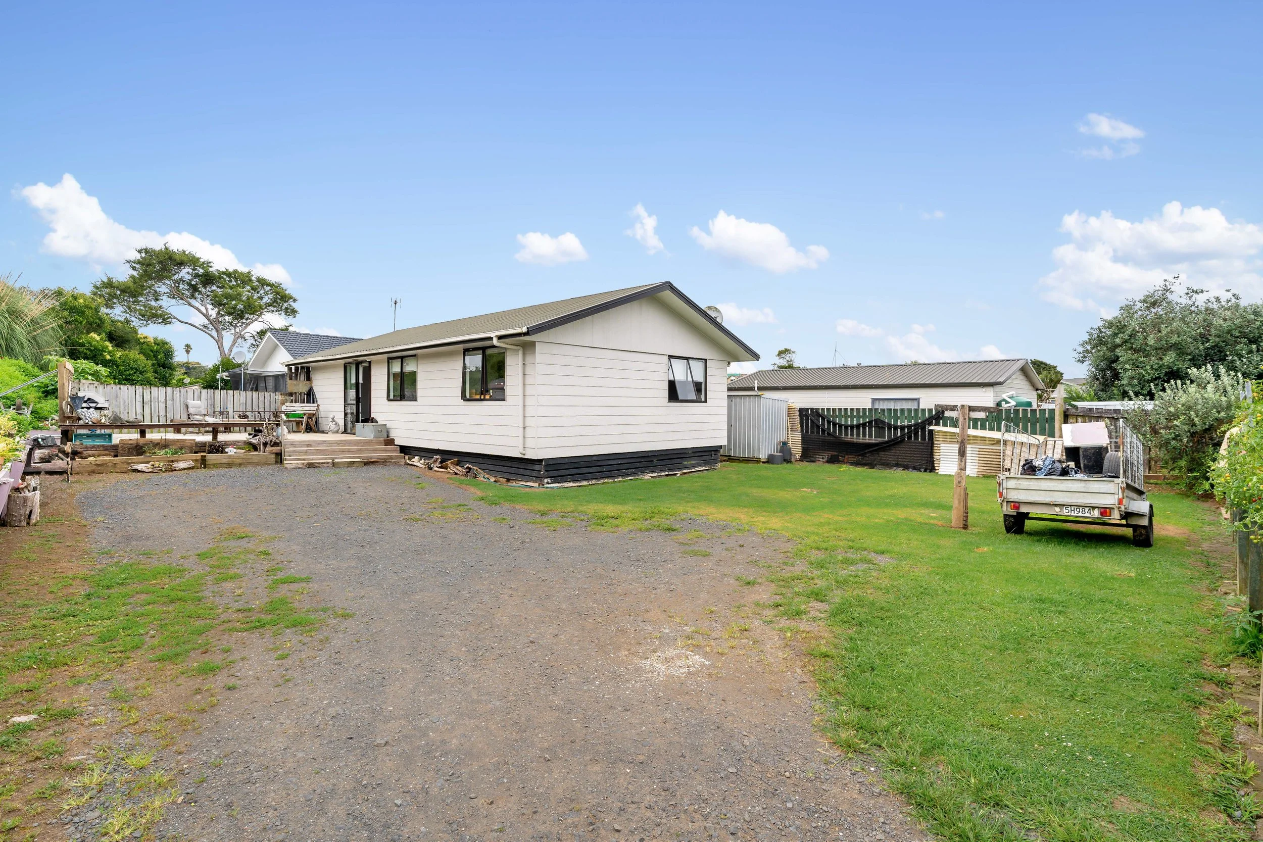 View of a house with a yard, a gravel driveway, and a lawn, with a truck parked on the grass and trees in the background.