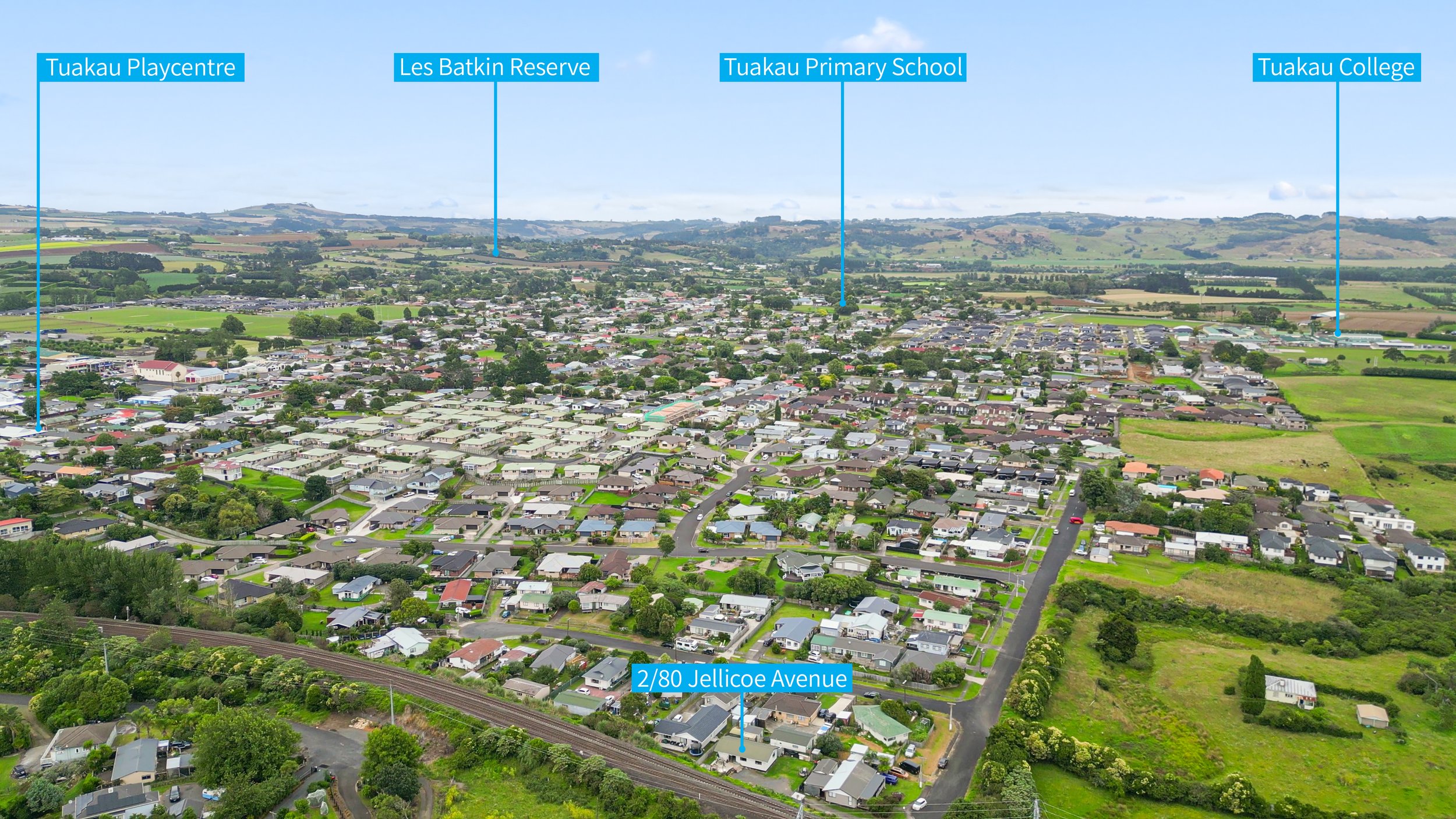 Aerial view of a suburban area with labeled locations including Tuakau Playcentre, Les Batkin Reserve, Tuakau Primary School, Tuakau College, and 2/80 Jellicoe Avenue. The area features a mix of houses, roads, greenery, and open fields.
