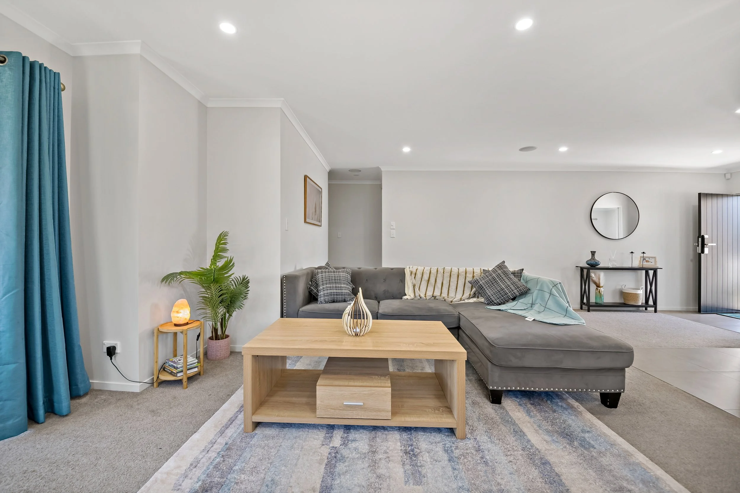 Living room with a sectional sofa, a wooden coffee table, a potted plant, a salt lamp, and a mirror on the wall.