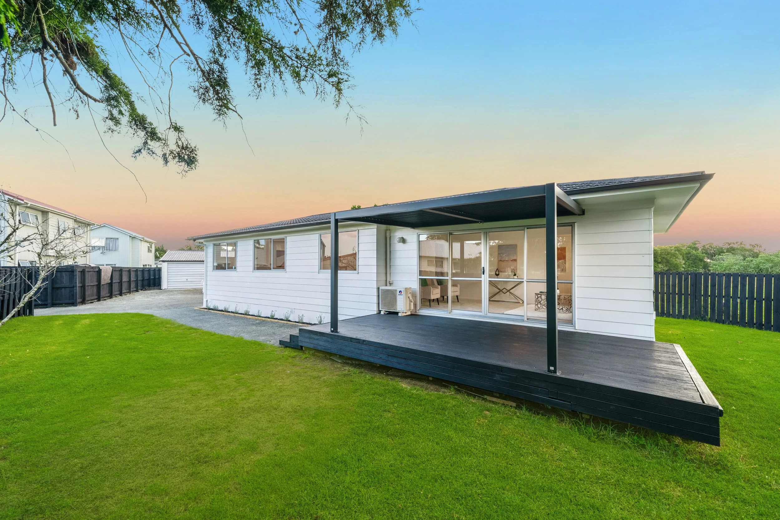 Modern white house with a black wooden deck porch and sliding glass doors on a green lawn at sunset.