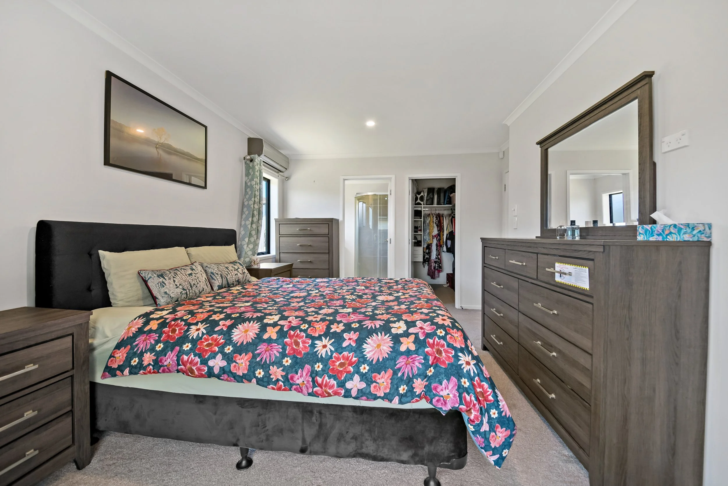 Modern bedroom with gray furniture, floral bedding, a black headboard, and a doorway to a walk-in closet.